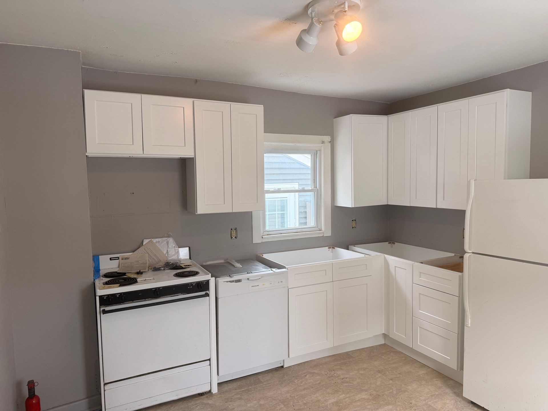 Small kitchen with white cabinets, gray walls, stove, sink, and a window above the counter.