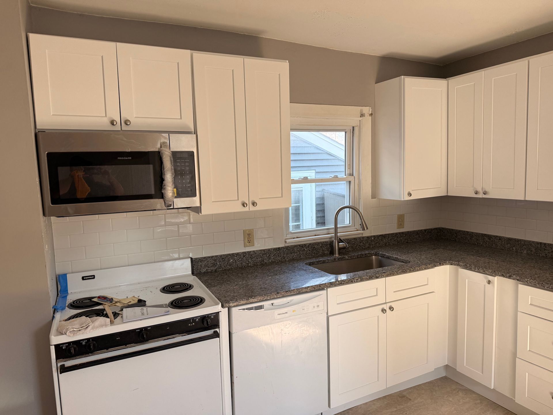 Bright kitchen with white cabinets, black countertops, stove, microwave, and a window over the sink.
