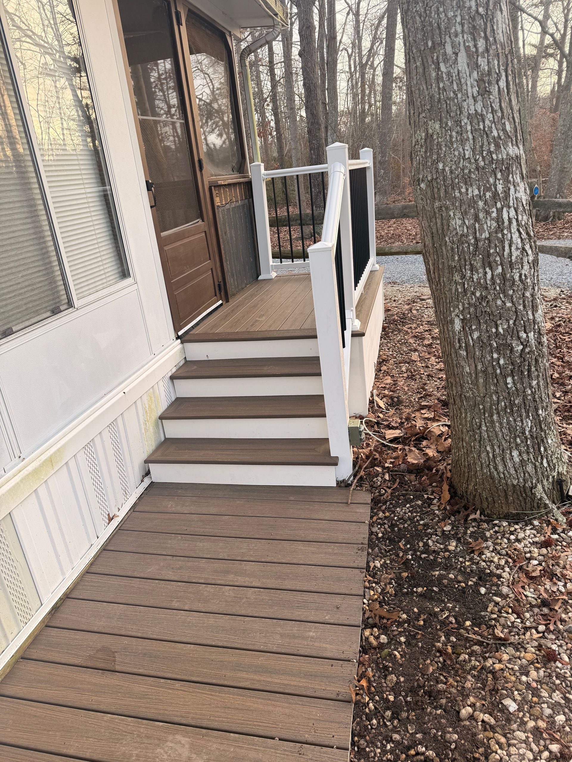 Wooden porch ramp and steps leading to a house entrance beside a large tree and leaf-covered ground