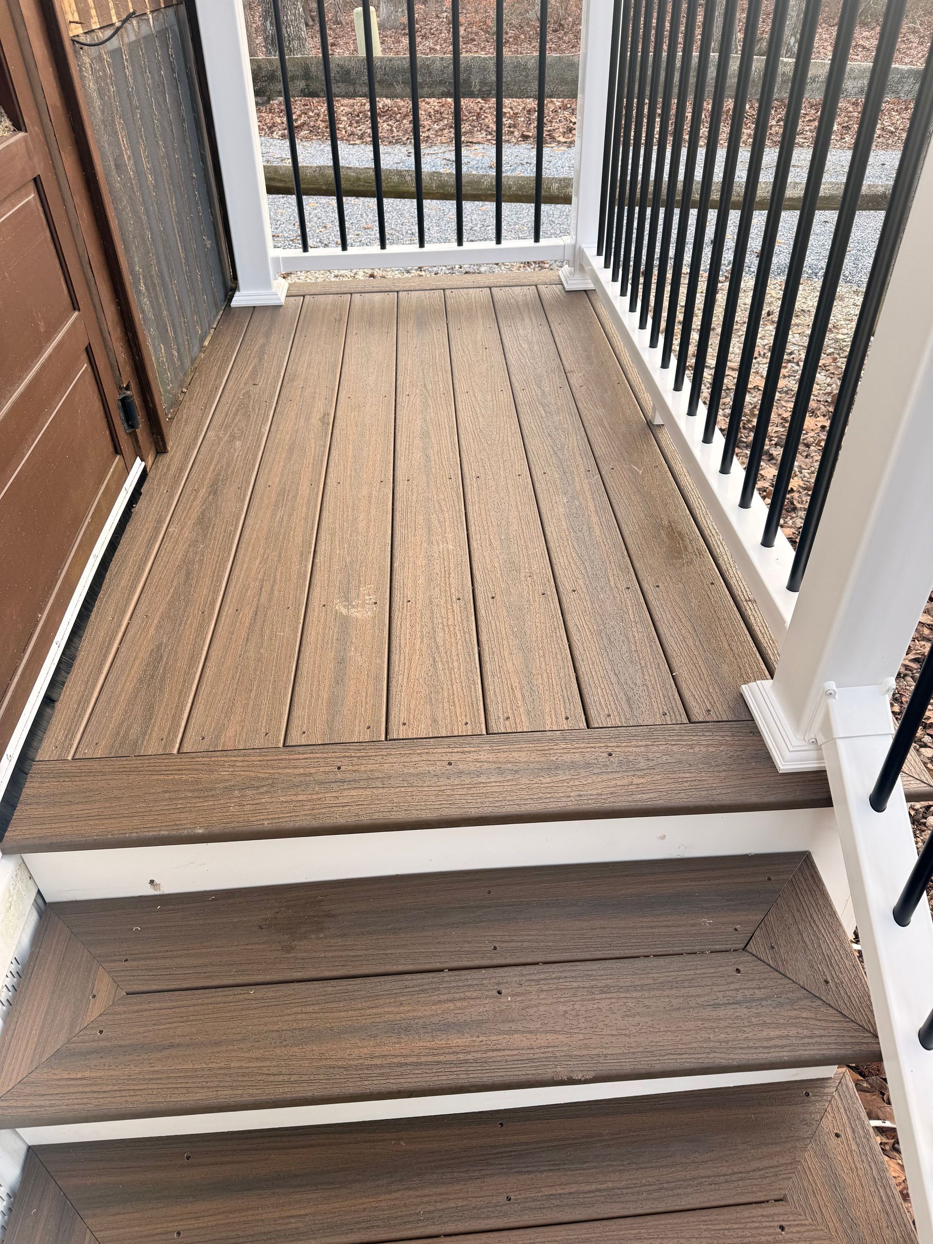 Small wooden porch deck with steps leading to a black metal gate and railings, seen from above.