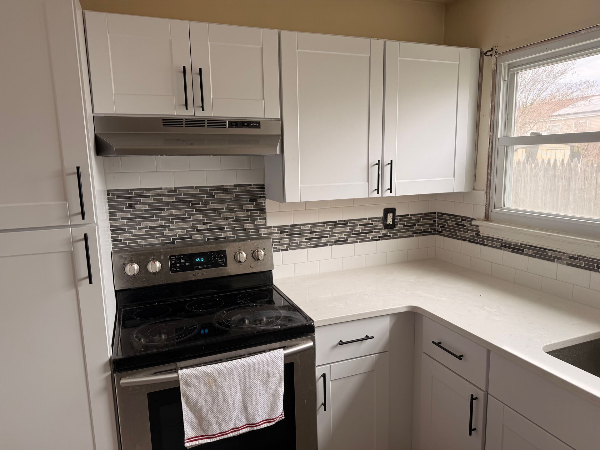 Bright kitchen with white cabinets, black stove, and white countertops by a window.