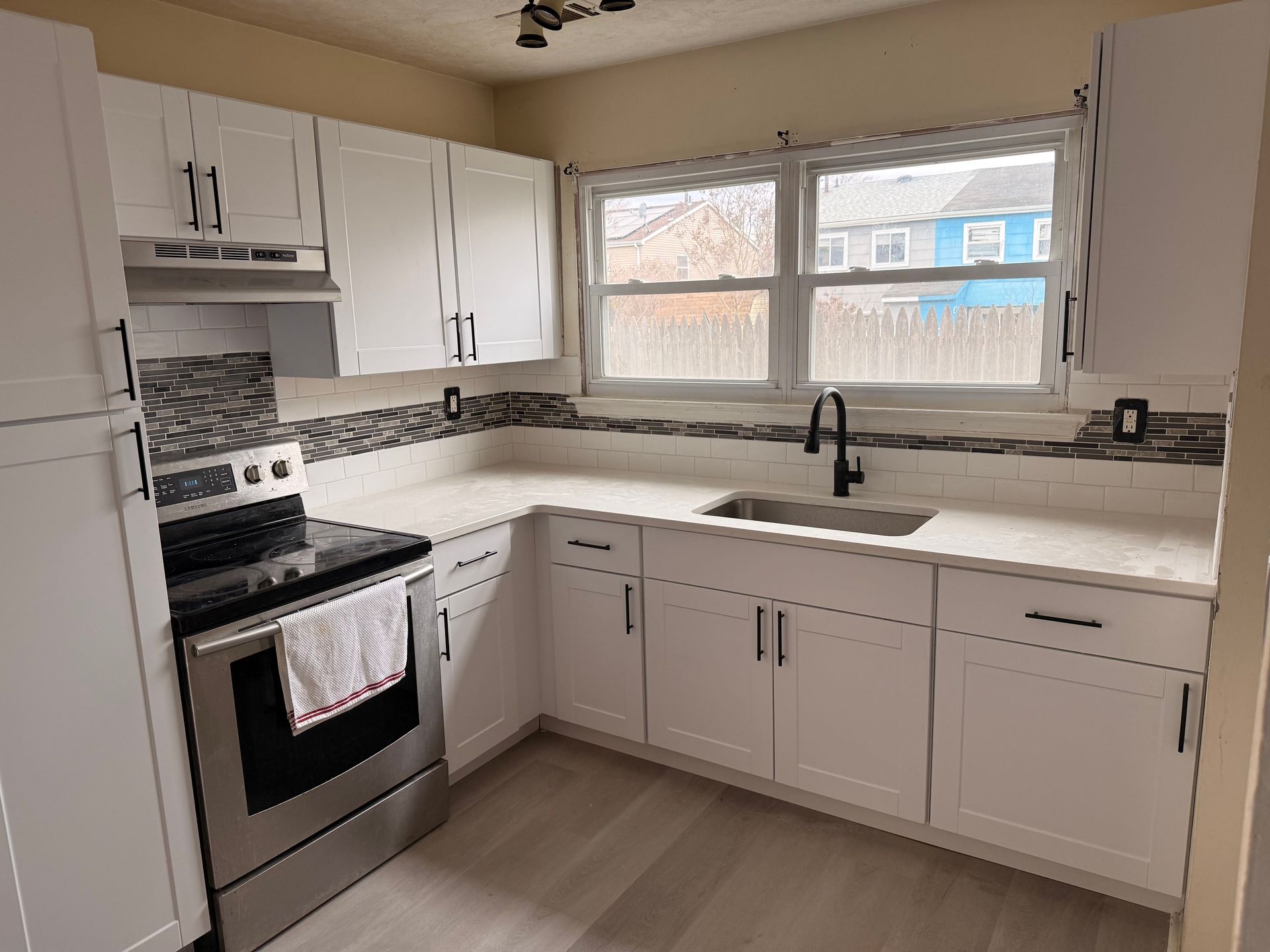 Bright kitchen with white cabinets, black stove, and large window over the sink.
