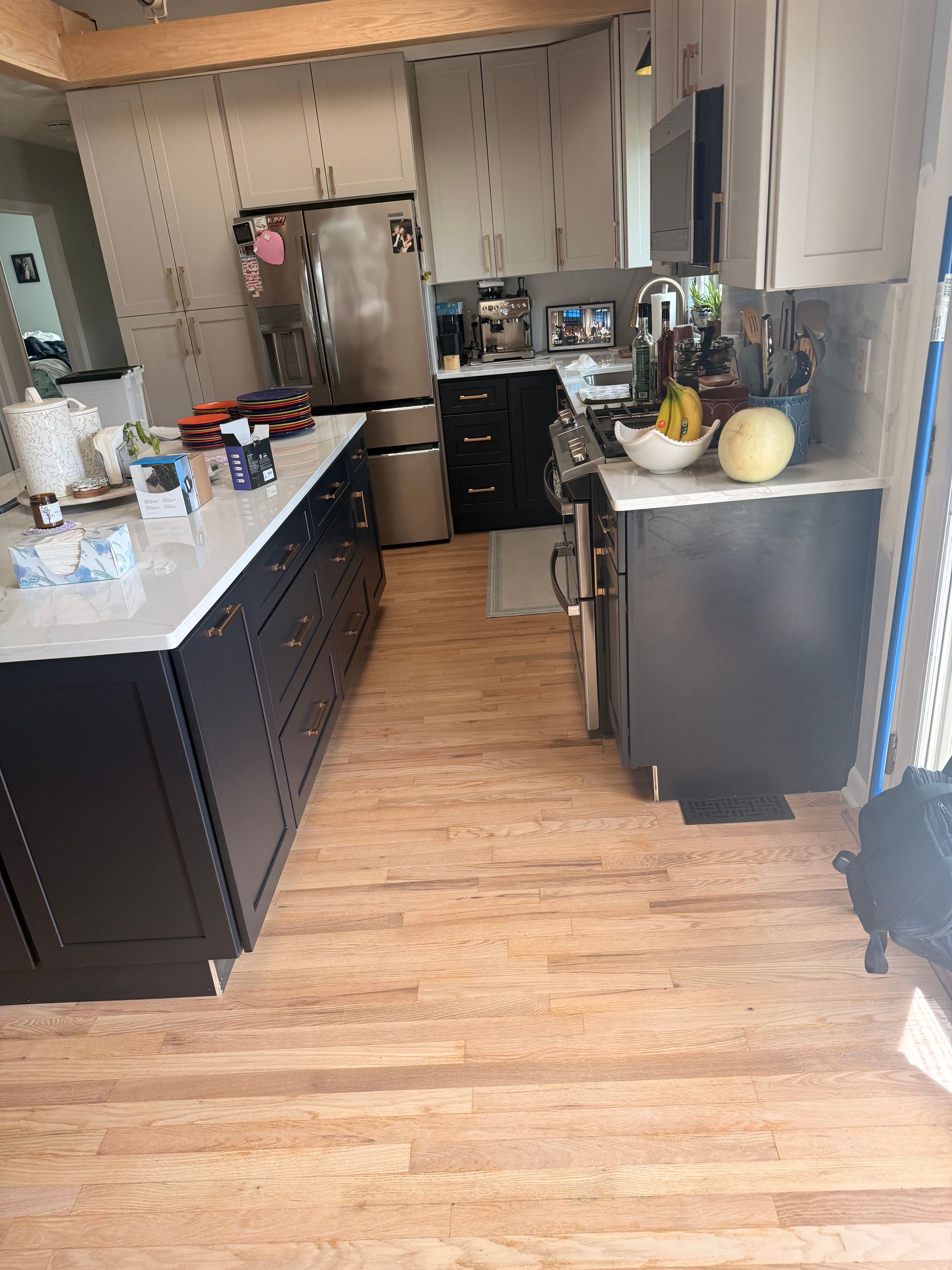 Kitchen with dark cabinets, white countertops, and wood flooring, viewed toward a refrigerator at the back.