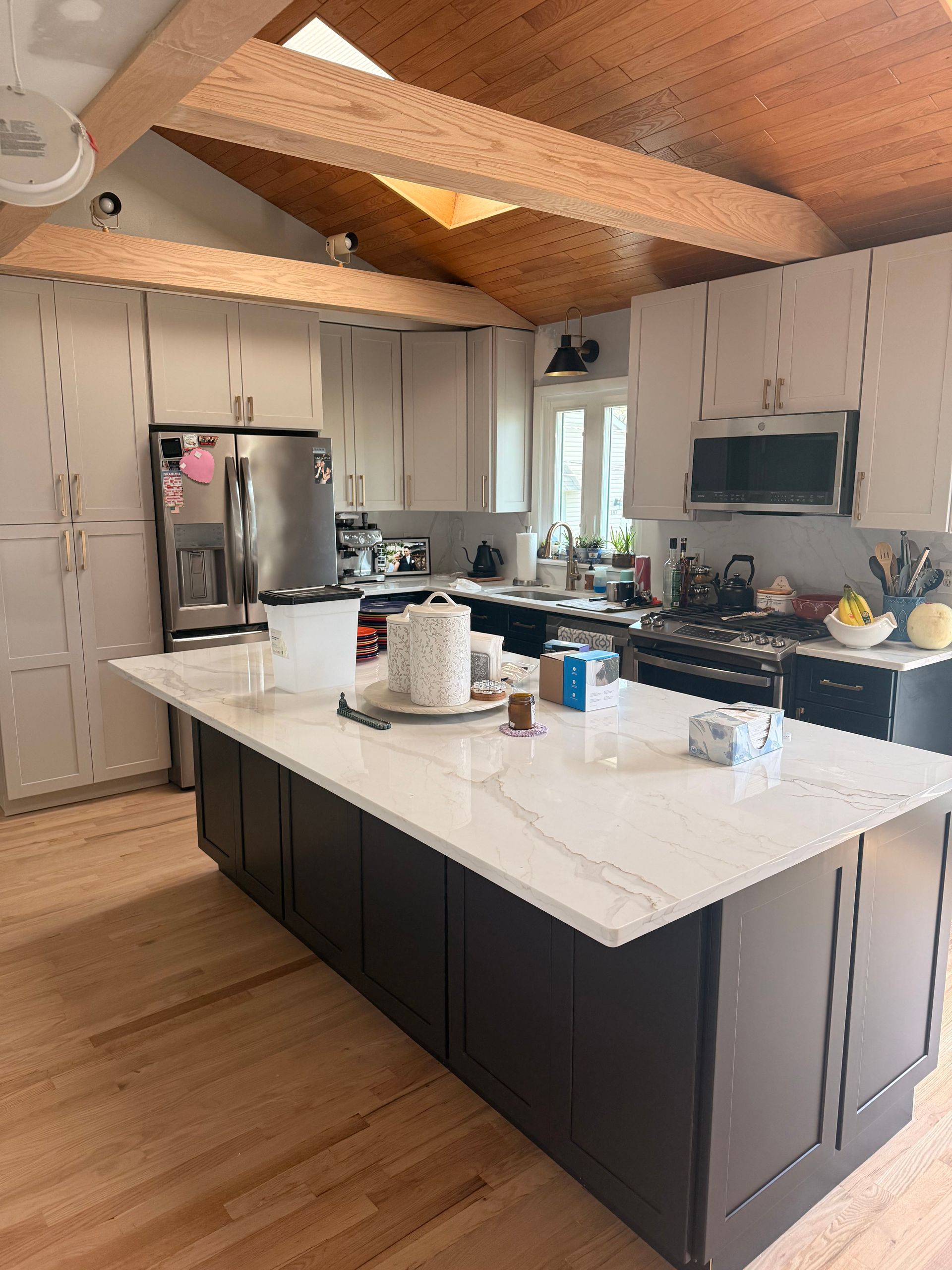 Modern kitchen with white island, stainless steel fridge, light wood ceiling beams, and cabinets.