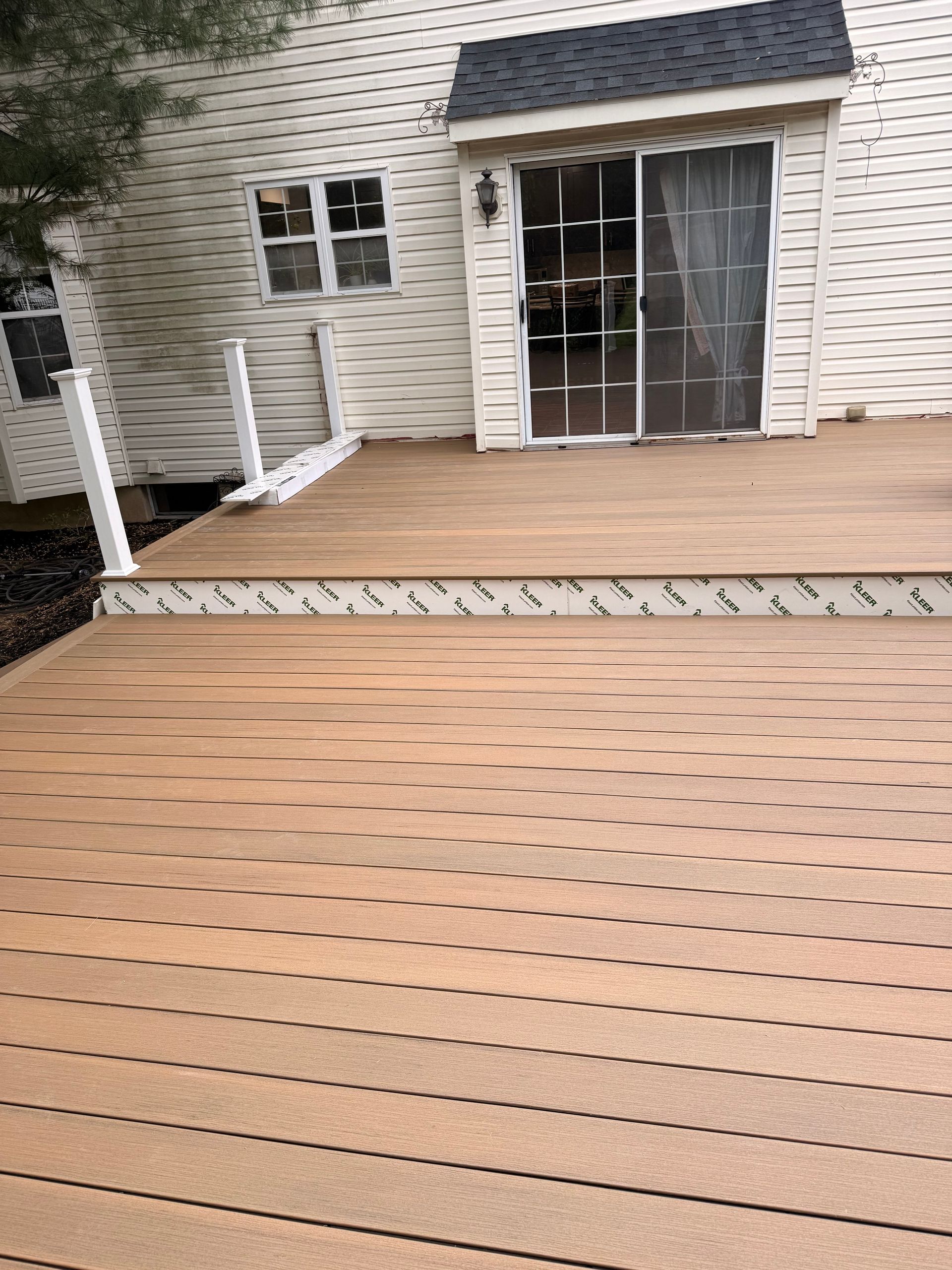 Wooden backyard deck with white railing, brick house wall, and sliding glass doors