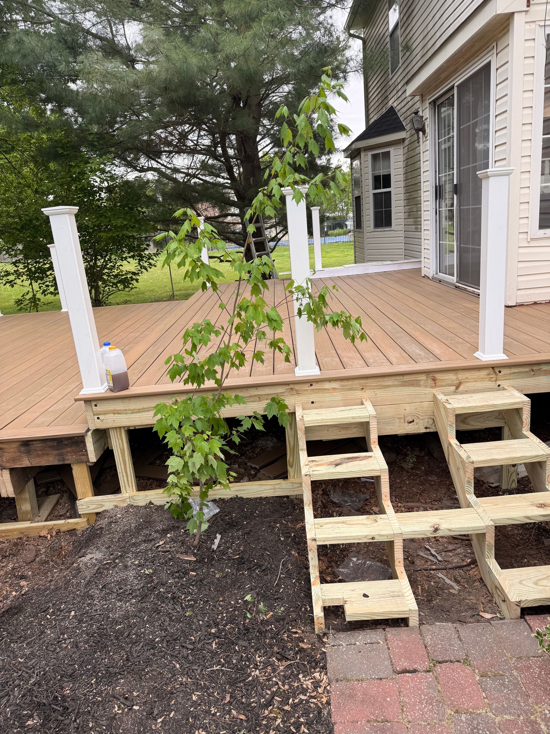Backyard deck with broken steps leading to a patio and house exterior