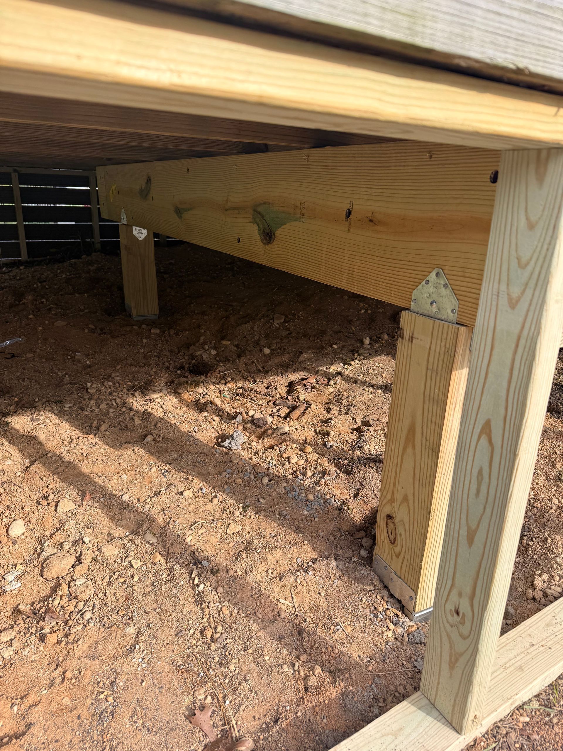 Under a raised wooden deck, showing support posts over bare dirt ground.
