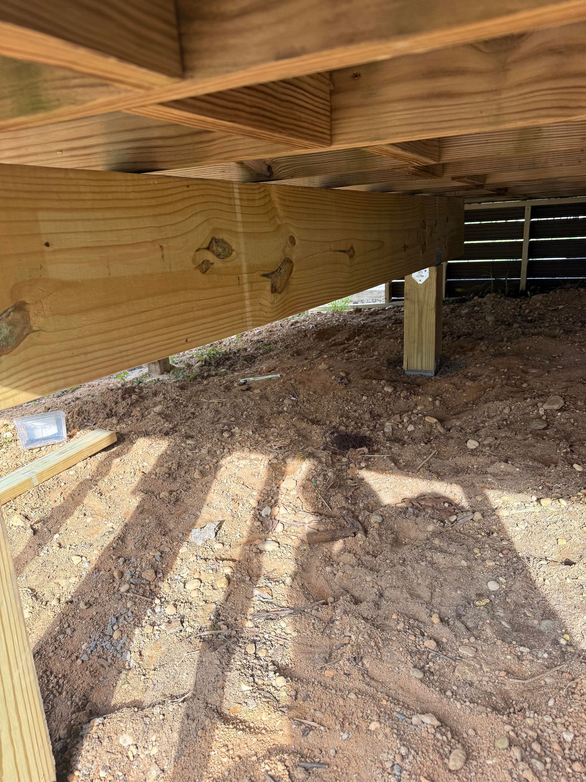 Underneath a wooden deck with gravel ground and sunlight shadows