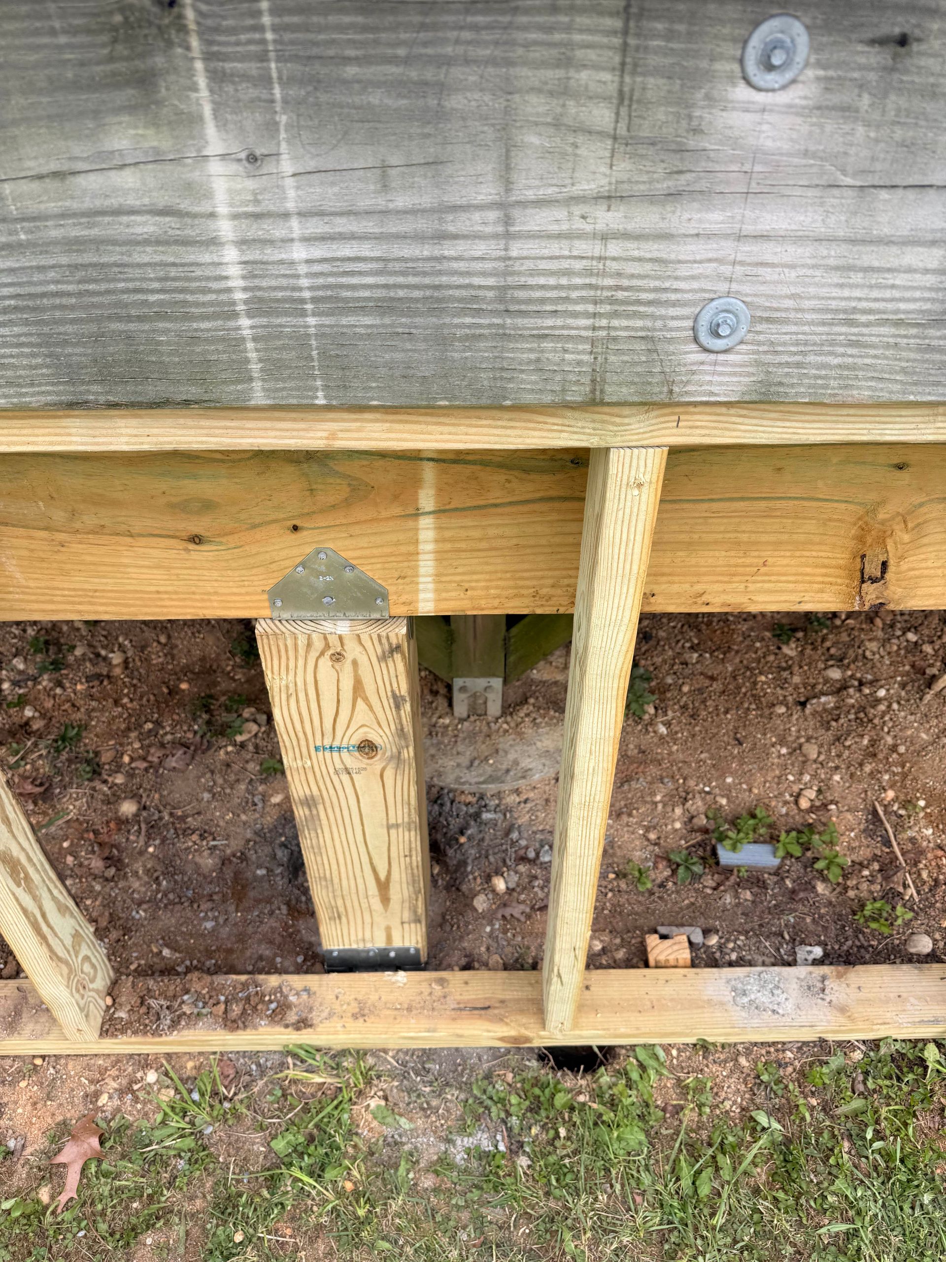 Wooden framing supports beneath a gray exterior wall, with soil and gravel visible below.