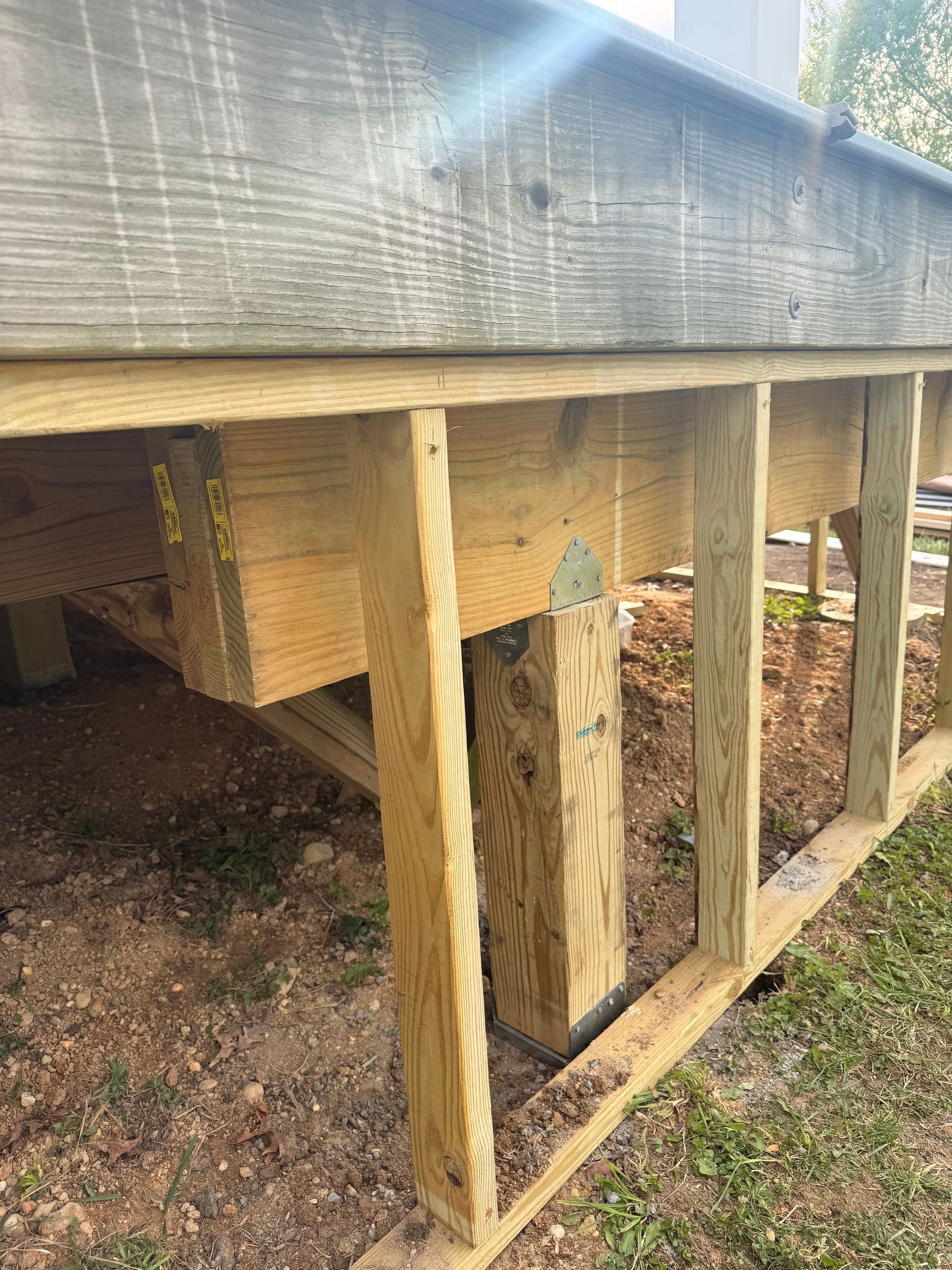 Raised wooden deck frame with vertical support posts and screened skirting outdoors