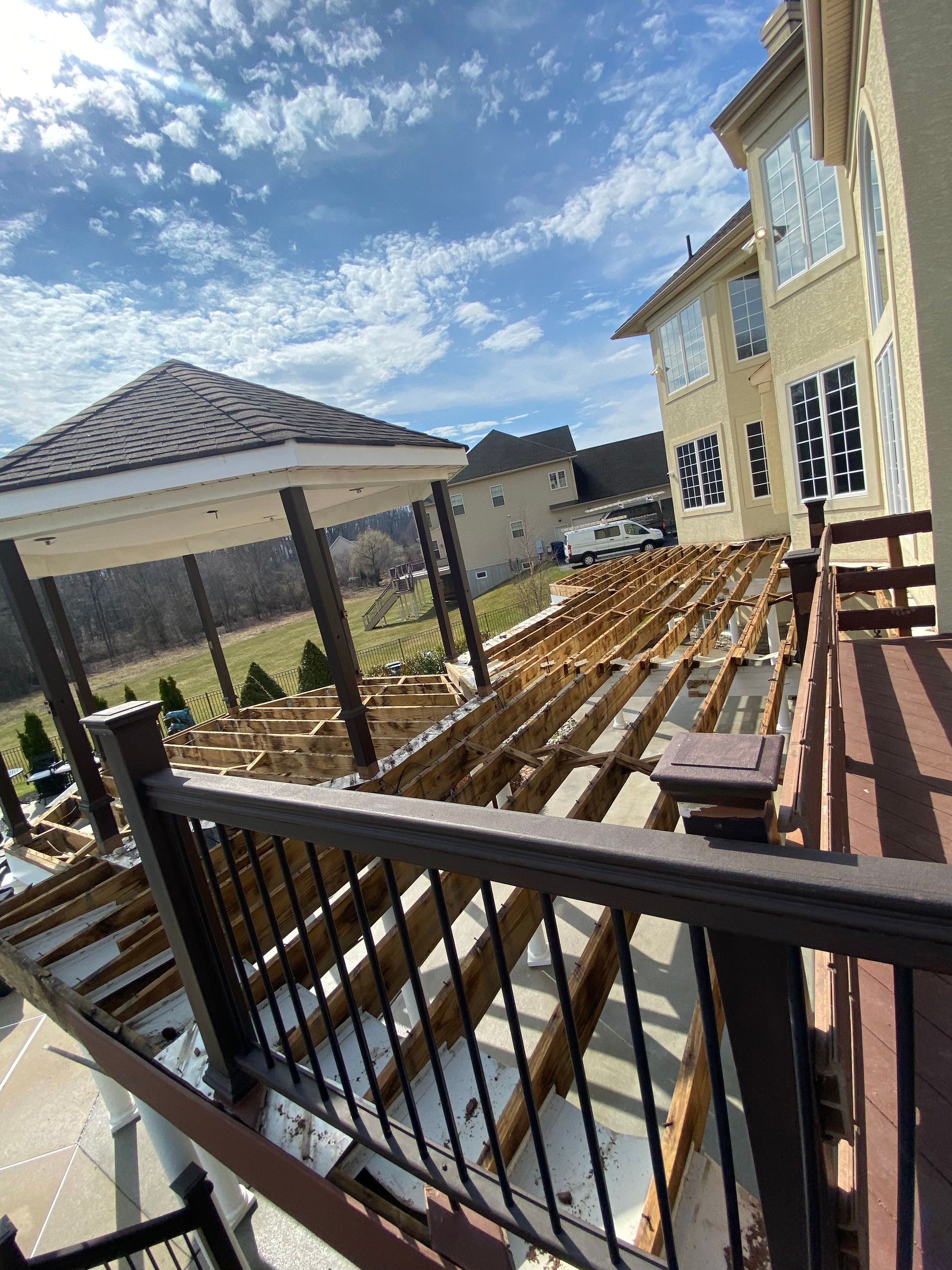 Backyard wooden deck under construction beside a yellow house, with a gazebo and blue sky.
