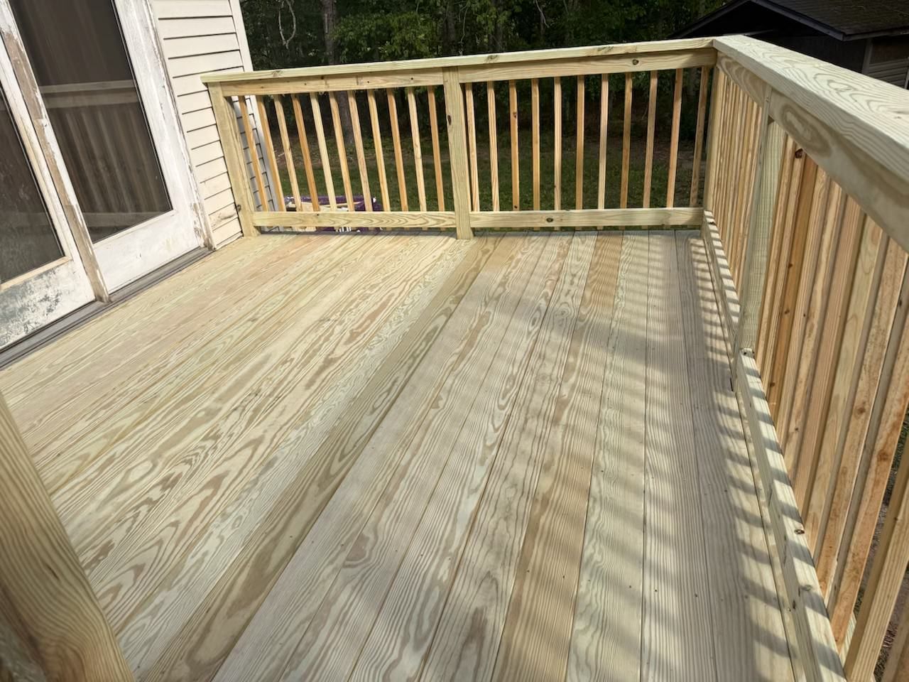 Wooden deck with railings and sunlit shadows beside a house