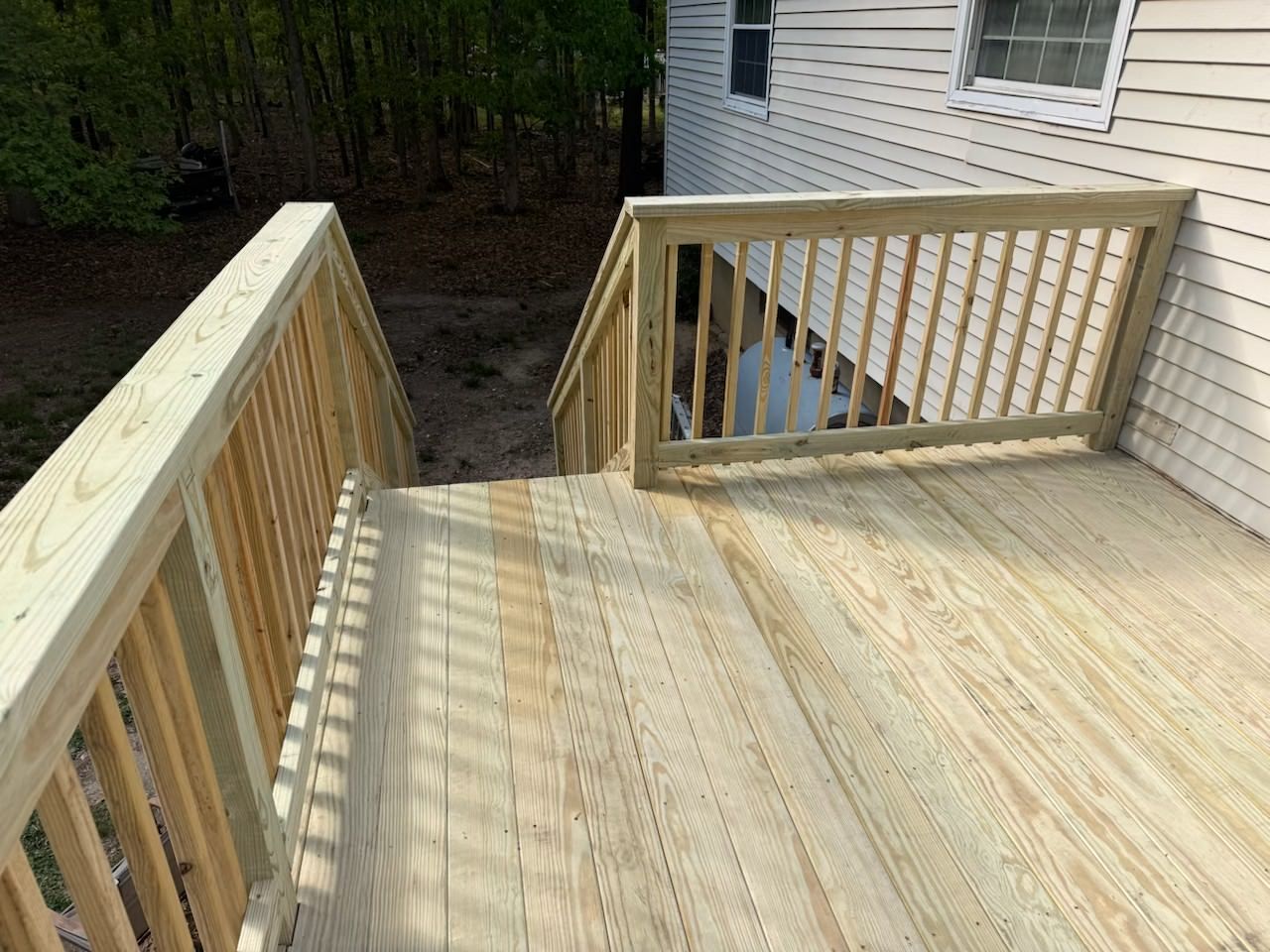 Wooden deck with railings and stairs beside a house, overlooking a wooded yard
