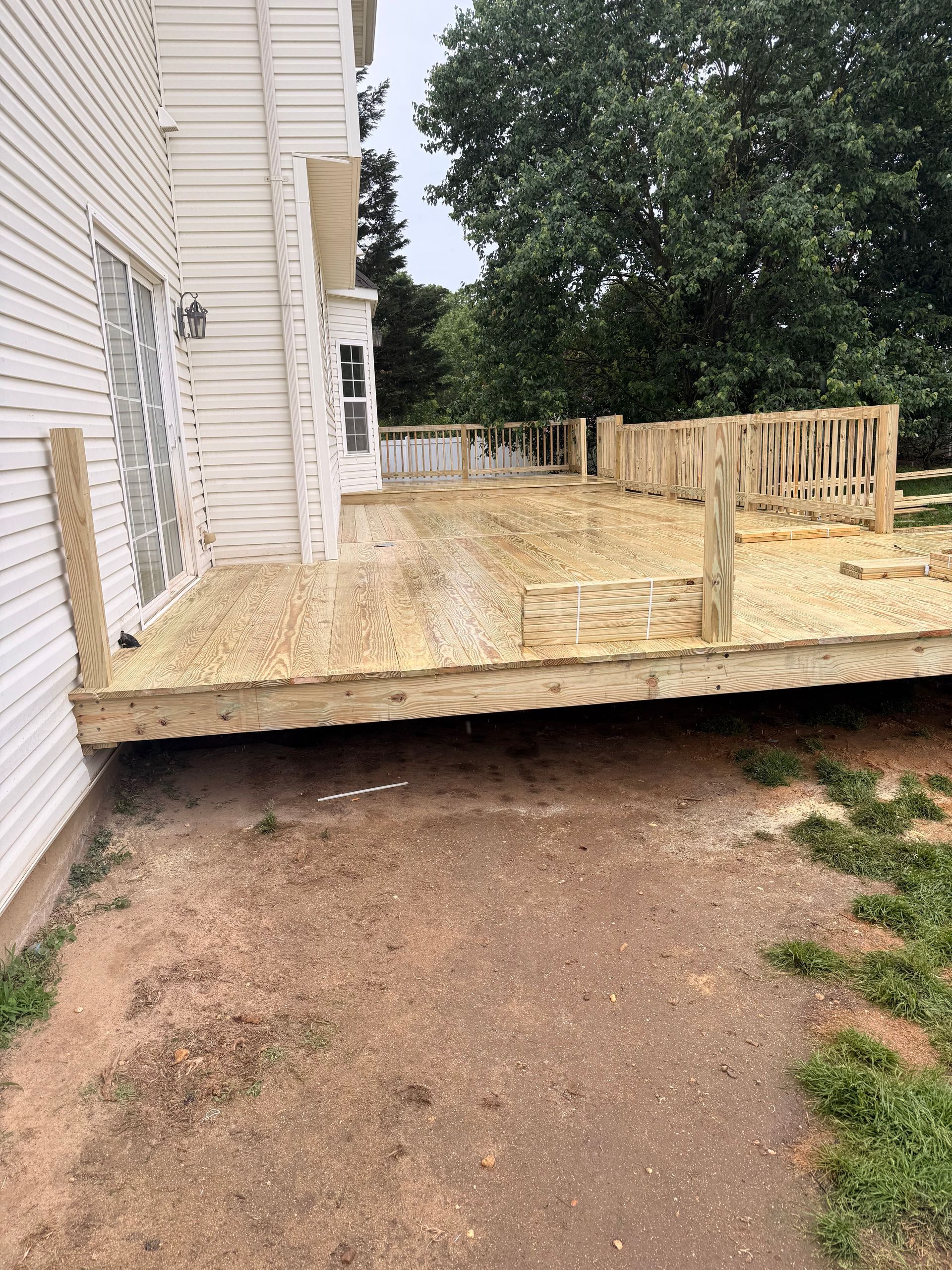 Partially built wooden deck beside a house, with exposed framing and no railing on the near side