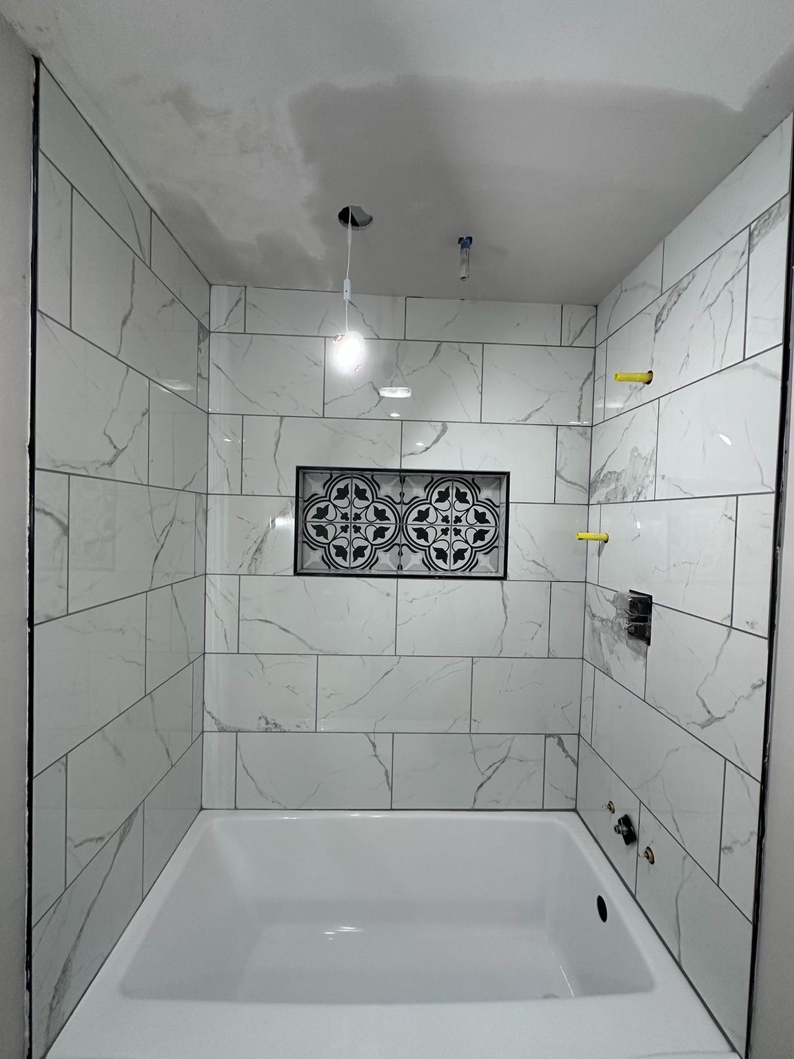 Newly tiled shower with white marble-look walls, bathtub, and a small window