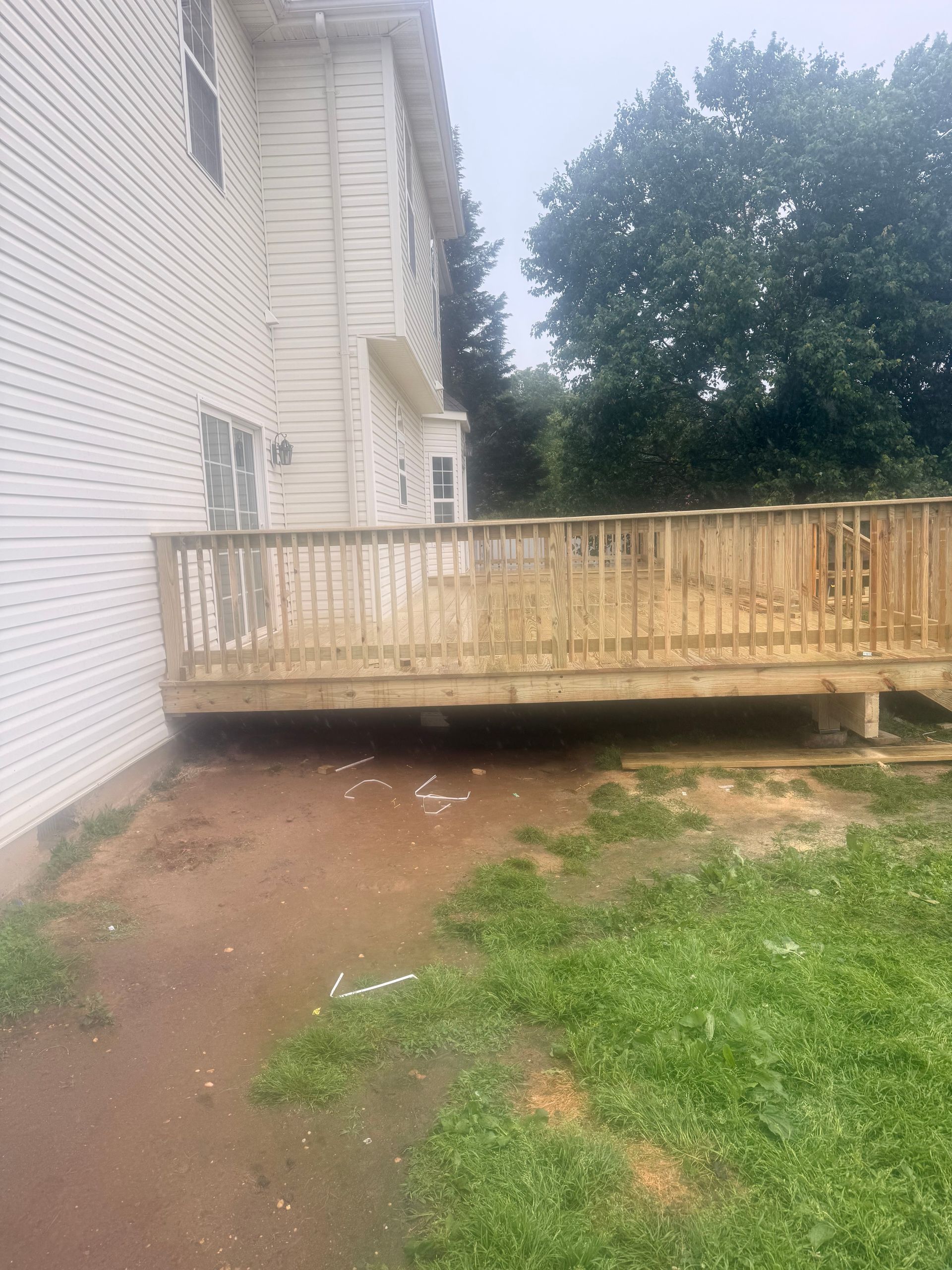 Wooden deck beside a white house, with muddy yard and trees in the background.