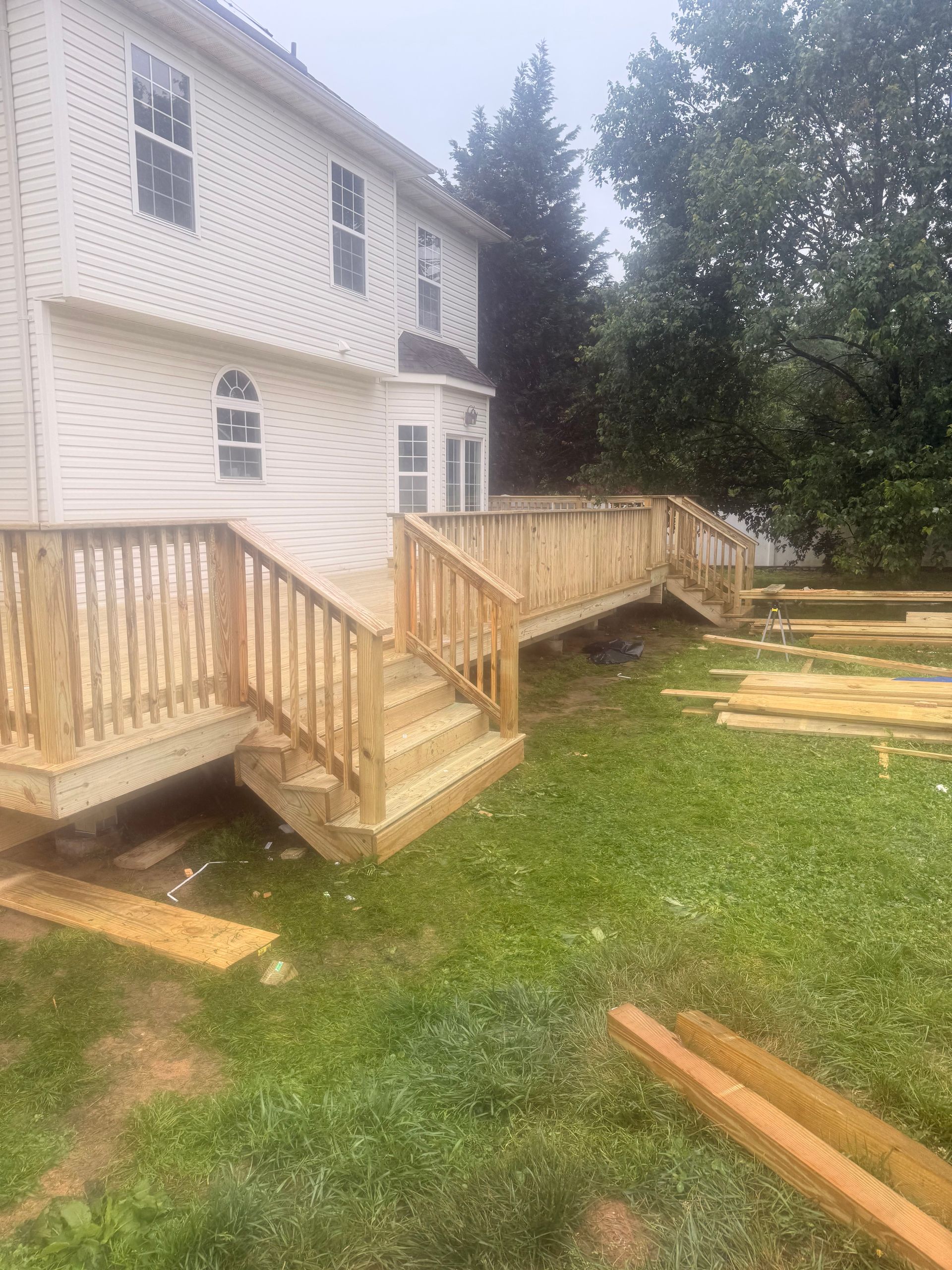Wooden ramp and steps beside a white house, with lumber stacked in the grassy yard.