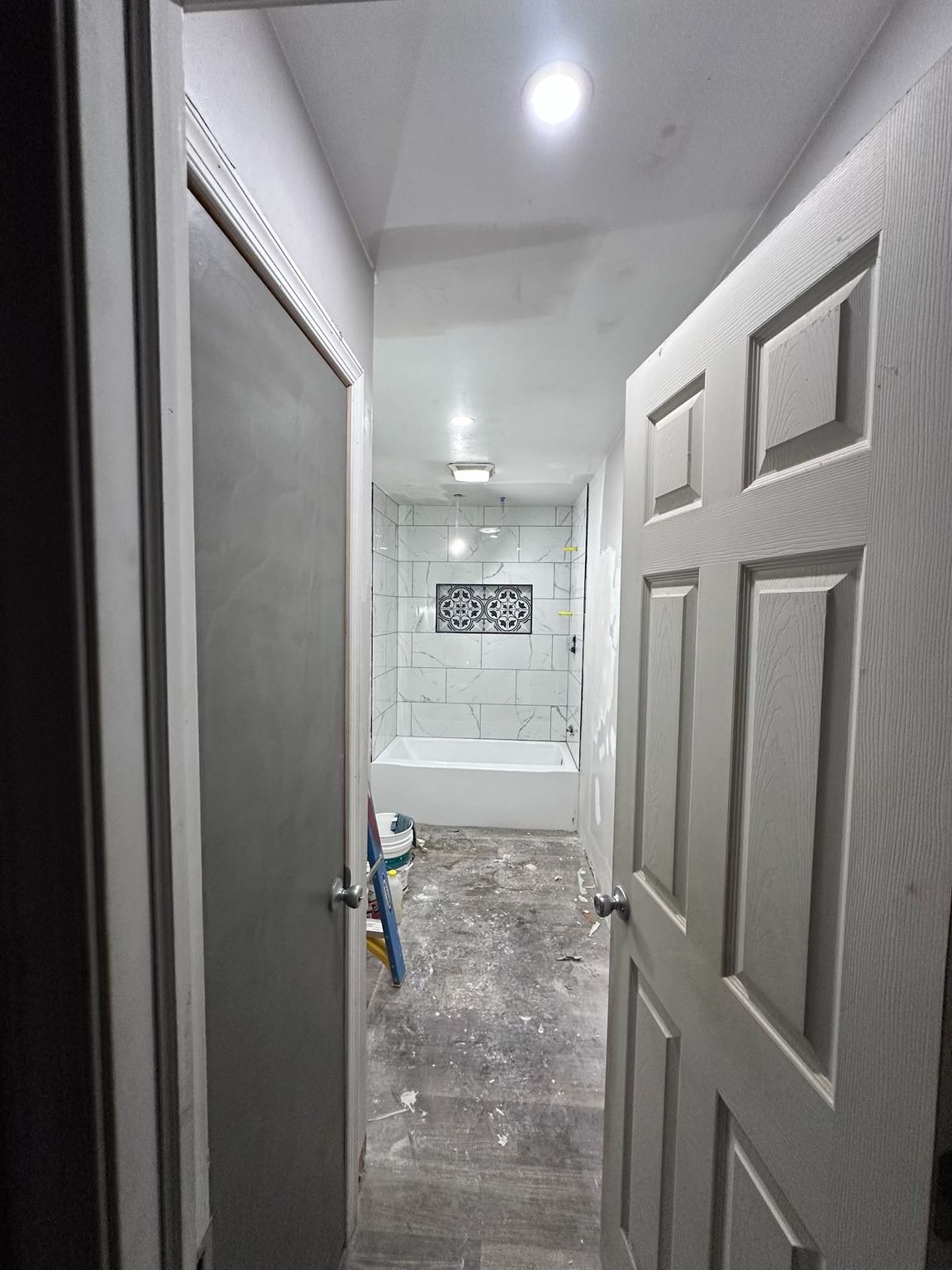 Narrow bathroom hallway with open doors, white walls, and a sink visible at the far end.