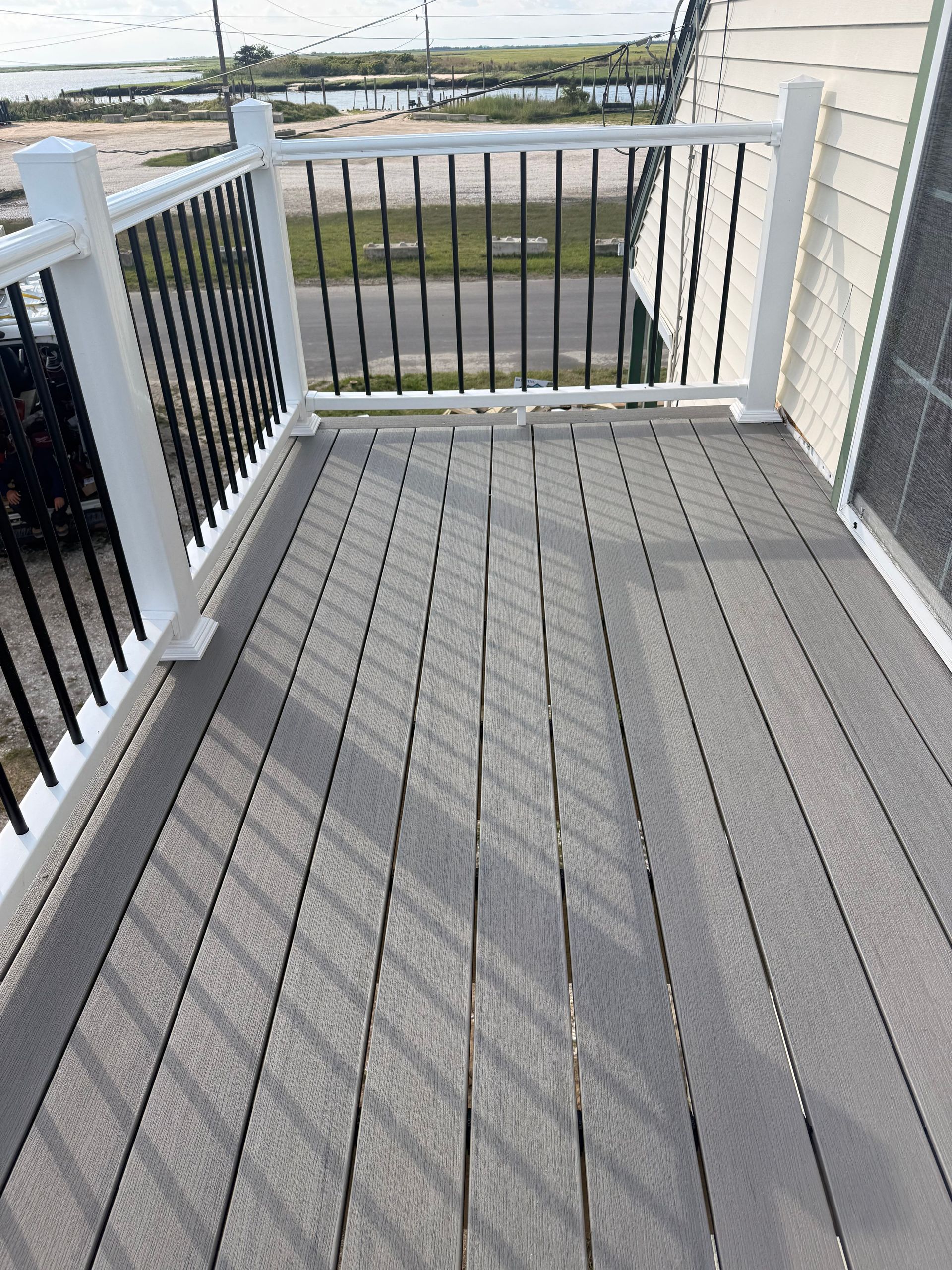 Gray deck with white railings overlooking a waterfront and road.