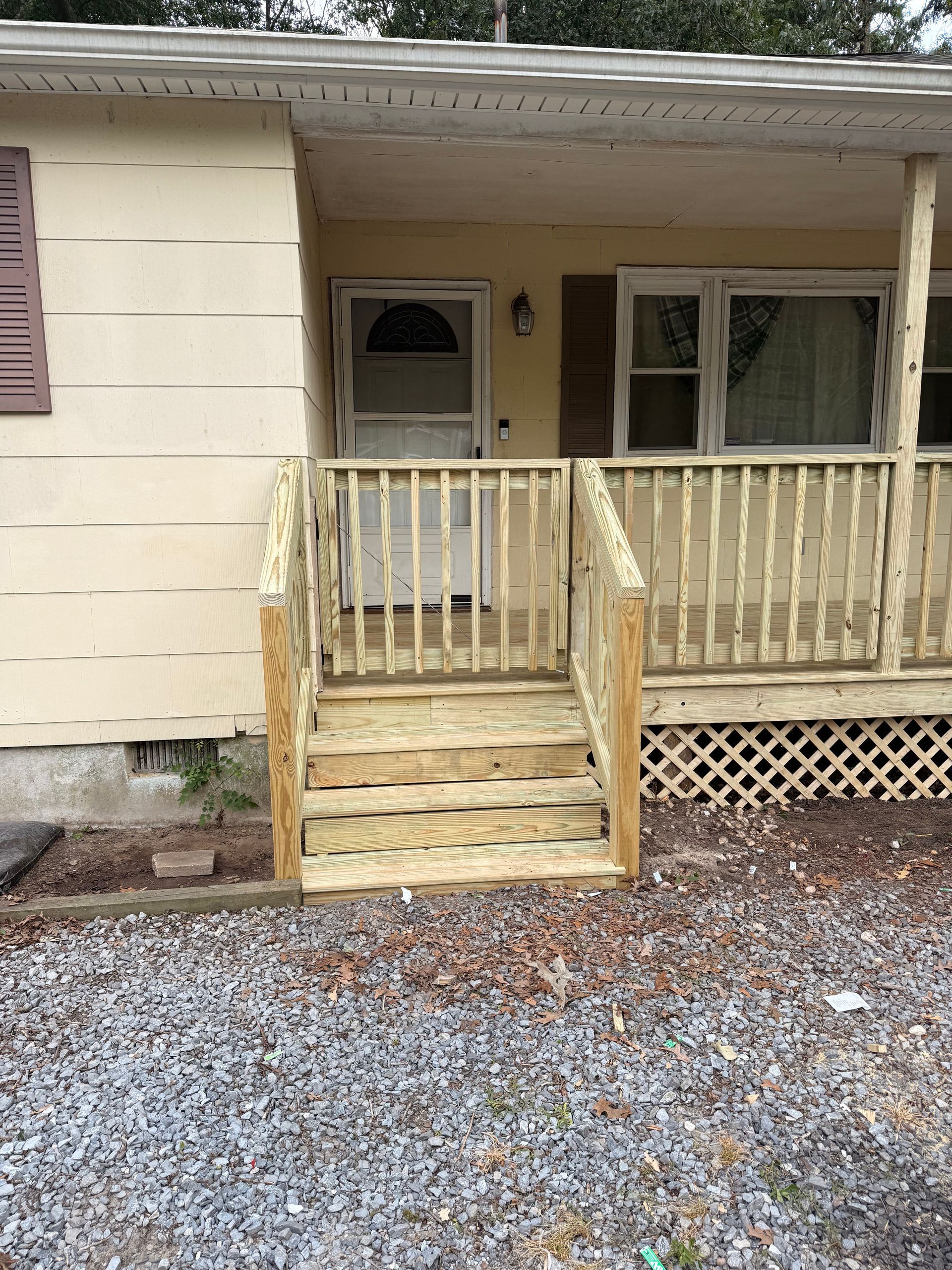 Front porch of a beige house with wooden steps, railing, a white door, and large windows.