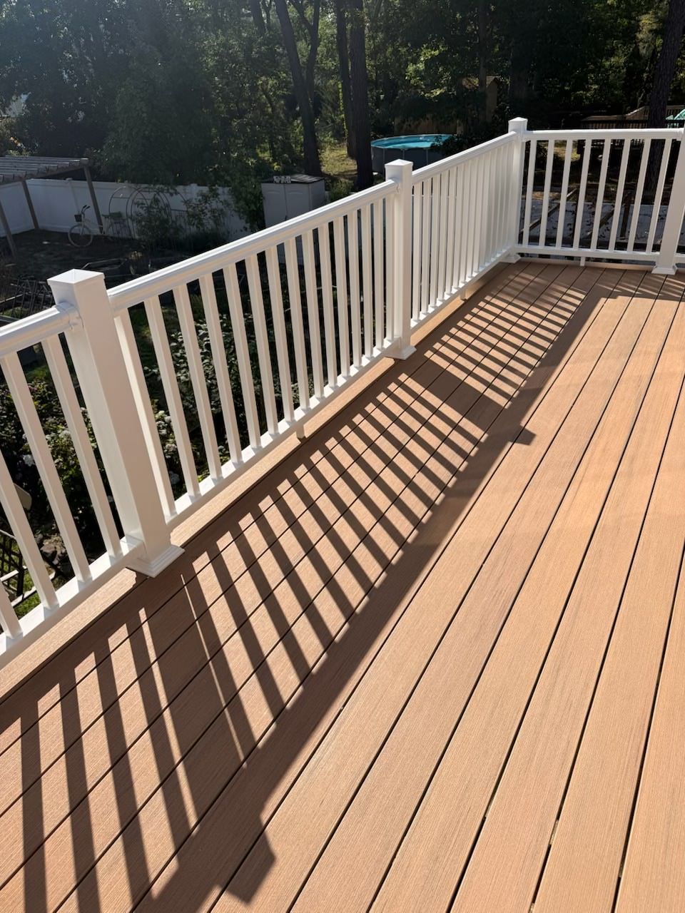 Wooden deck with white railing casting long striped shadows in bright sunlight.