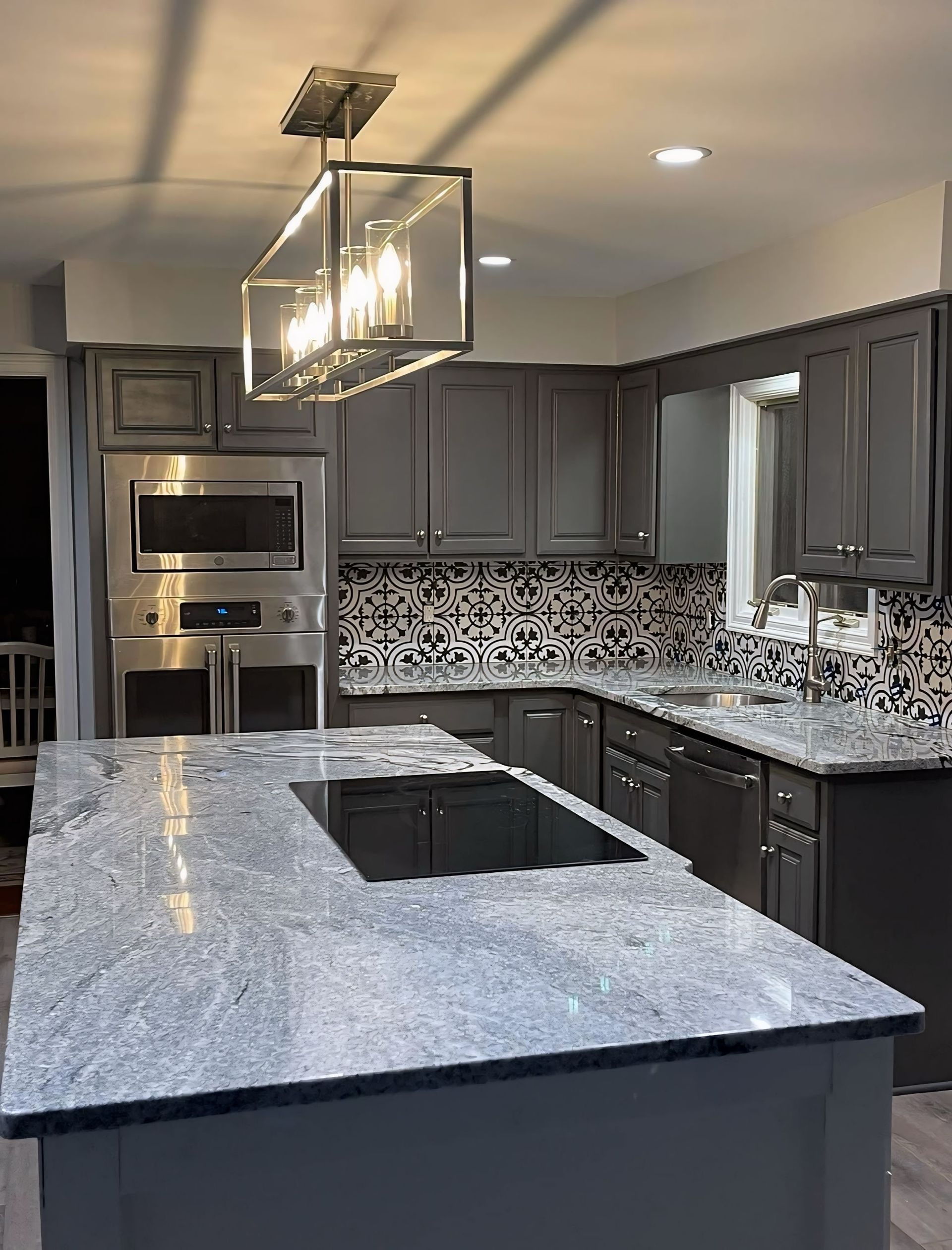 Modern kitchen with gray cabinets, stainless appliances, speckled countertops, and a large island under pendant lights