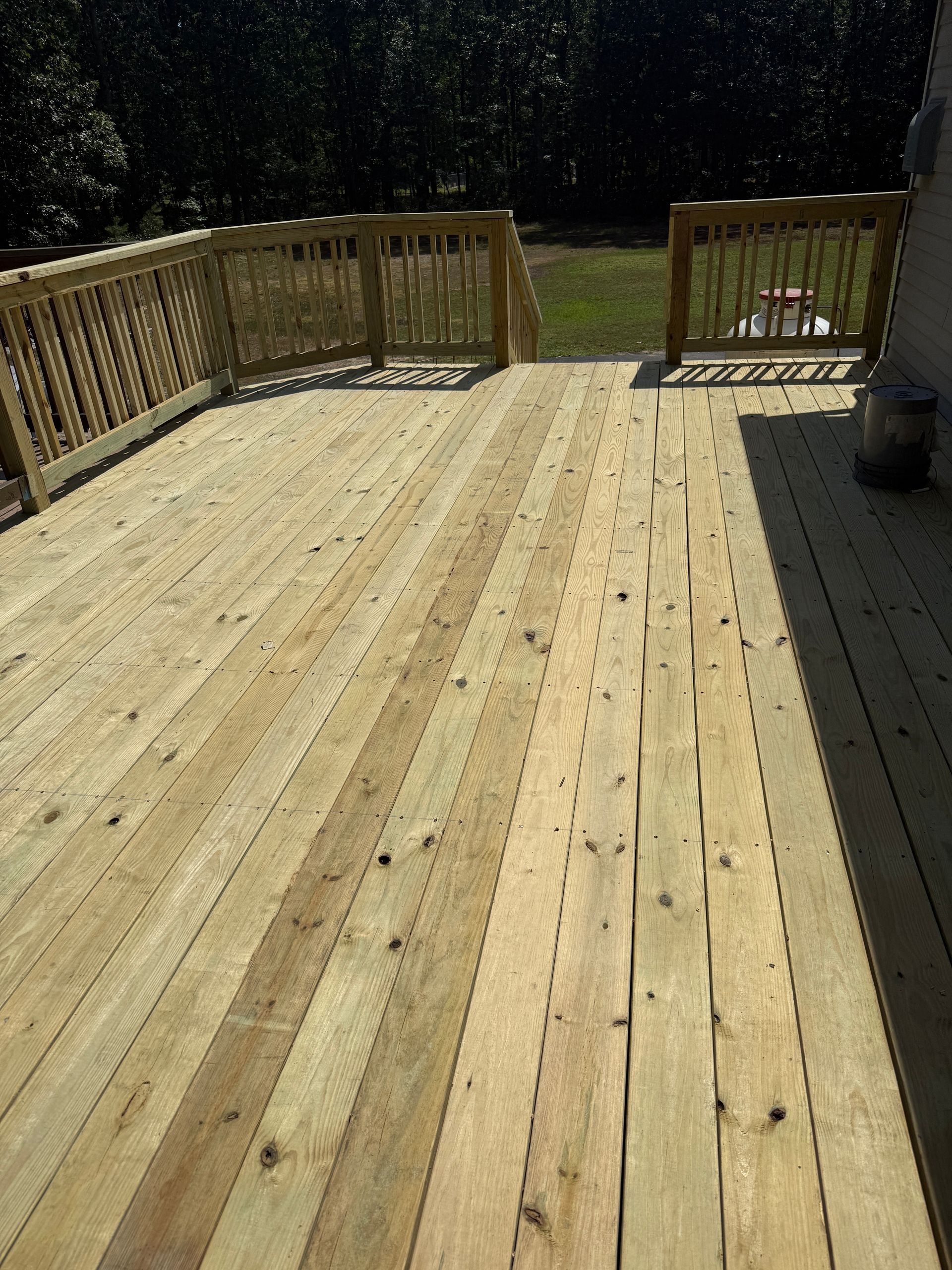 Wooden deck with railings and steps leading to a grassy yard in bright sunlight