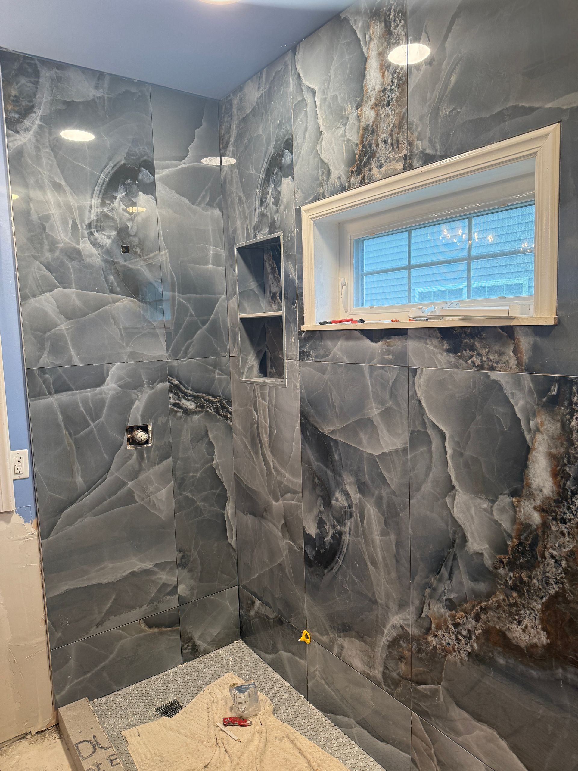 Finished bathroom shower with gray stone tile and a small window.