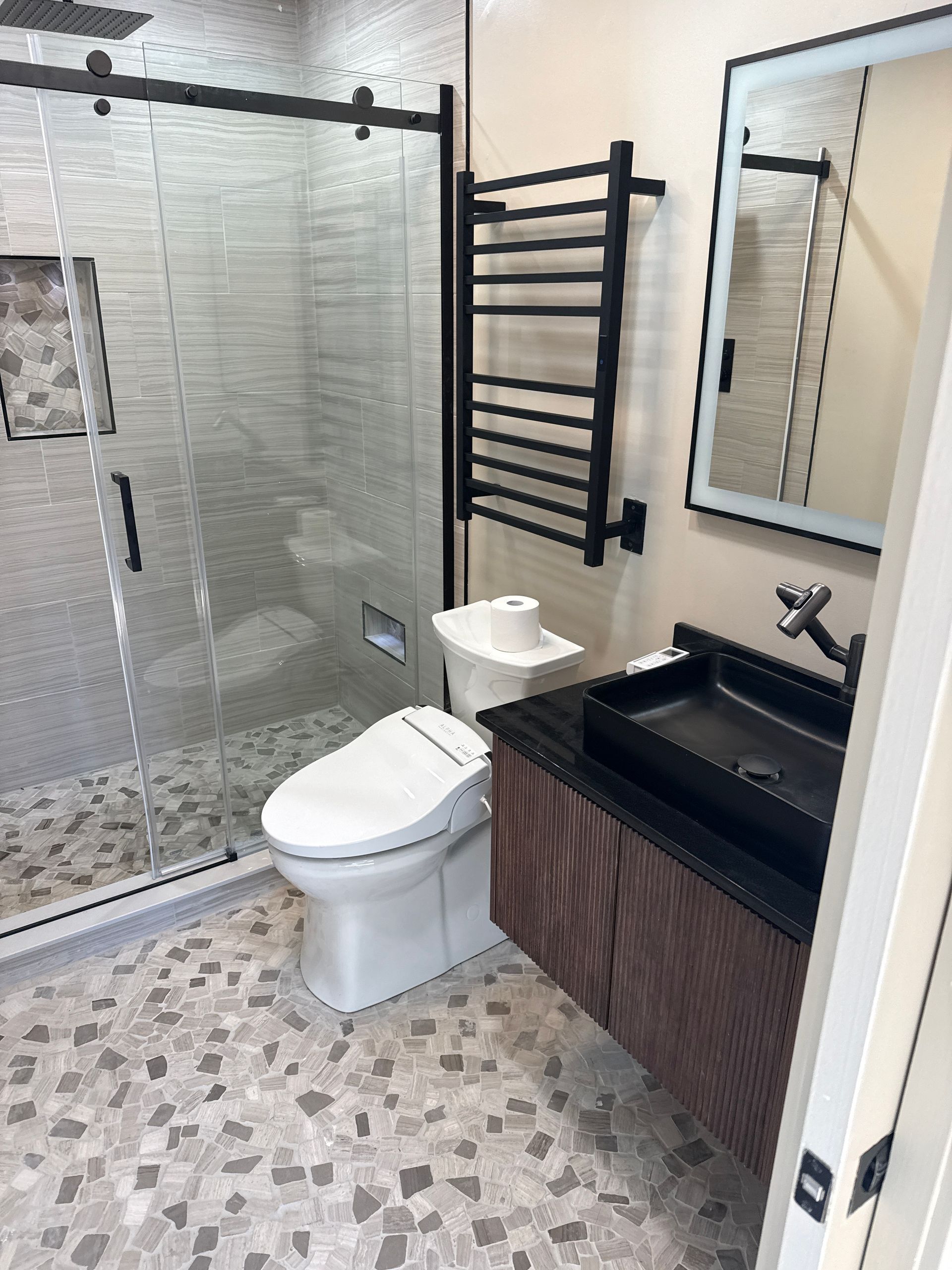 Modern bathroom with glass shower, toilet, black vanity, and mosaic tile floor.