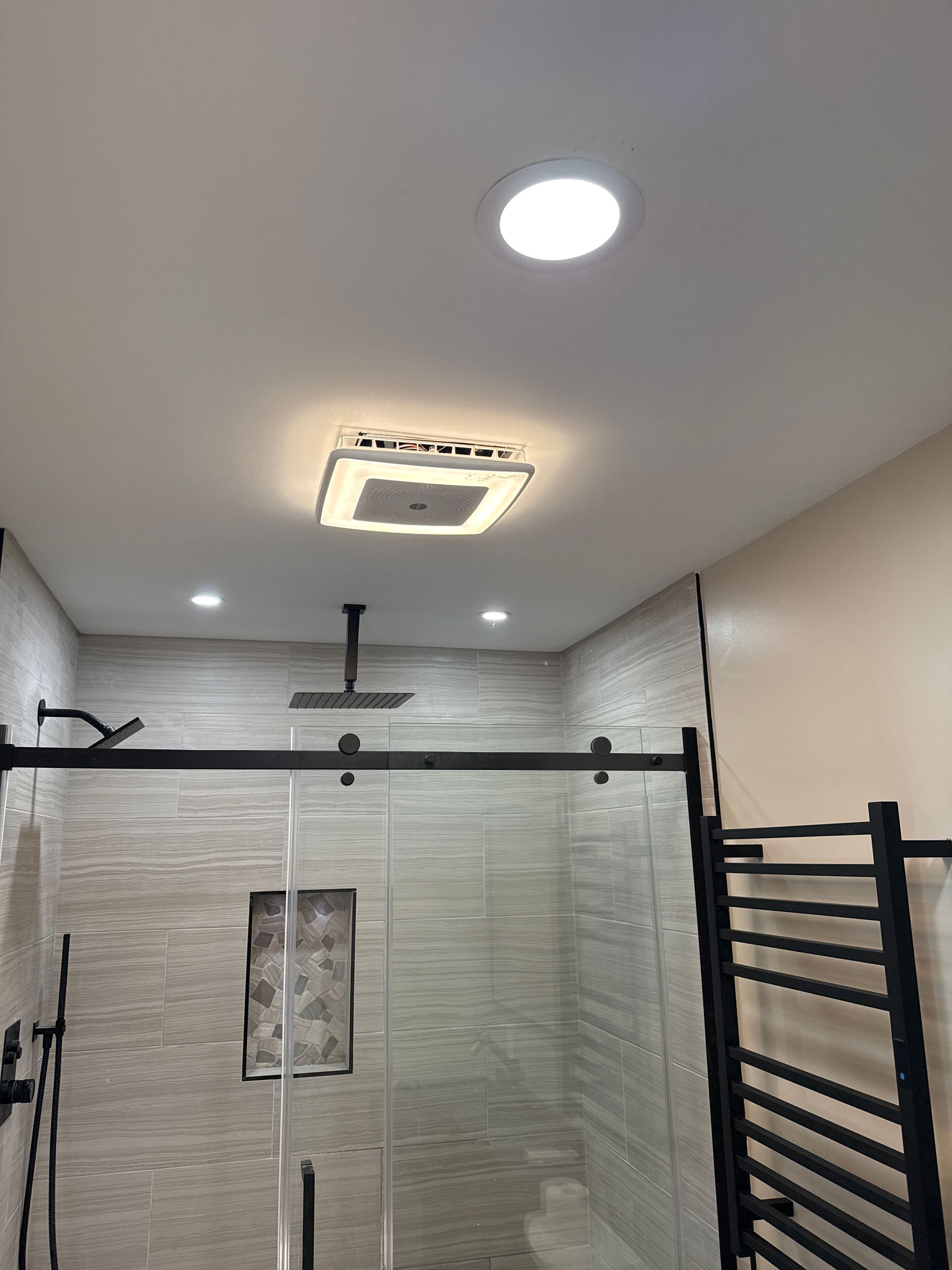Bright bathroom shower with black fixtures, beige tile walls, and ceiling lights