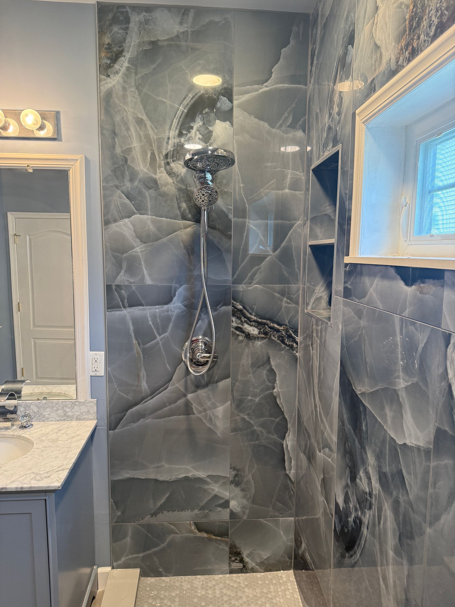 Modern bathroom shower with dark stone tile, glass enclosure, and a vanity mirror on the left