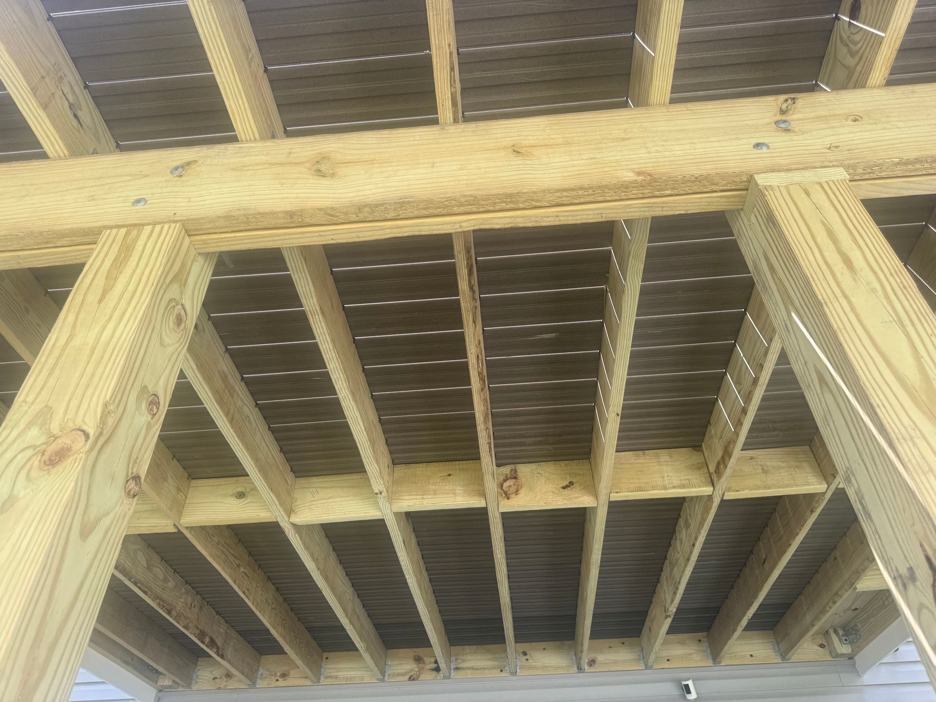 Wooden deck framing viewed from below, showing joists and beams against a bright sky.