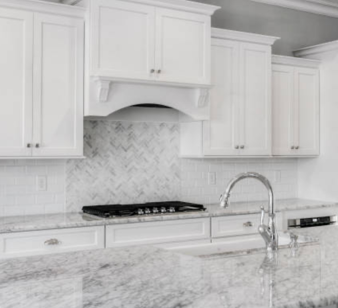 Bright white kitchen with marble countertops, tiled backsplash, gas range, and chrome faucet