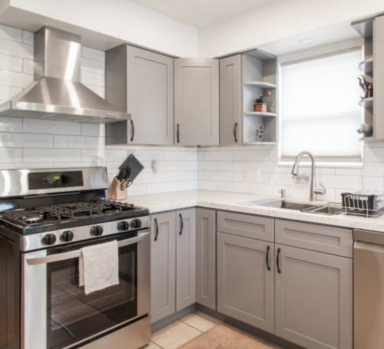Modern gray kitchen with stainless steel stove, white tile backsplash, and corner sink window