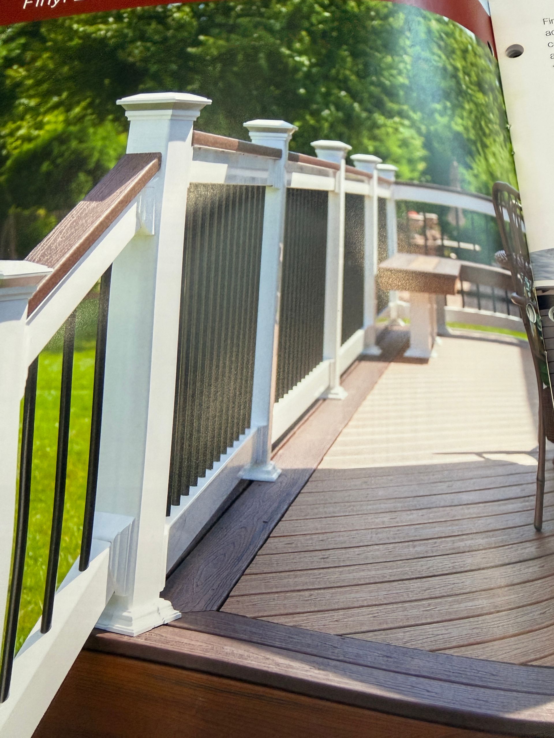 Wooden boardwalk with white railings curving through a green, sunny outdoor setting