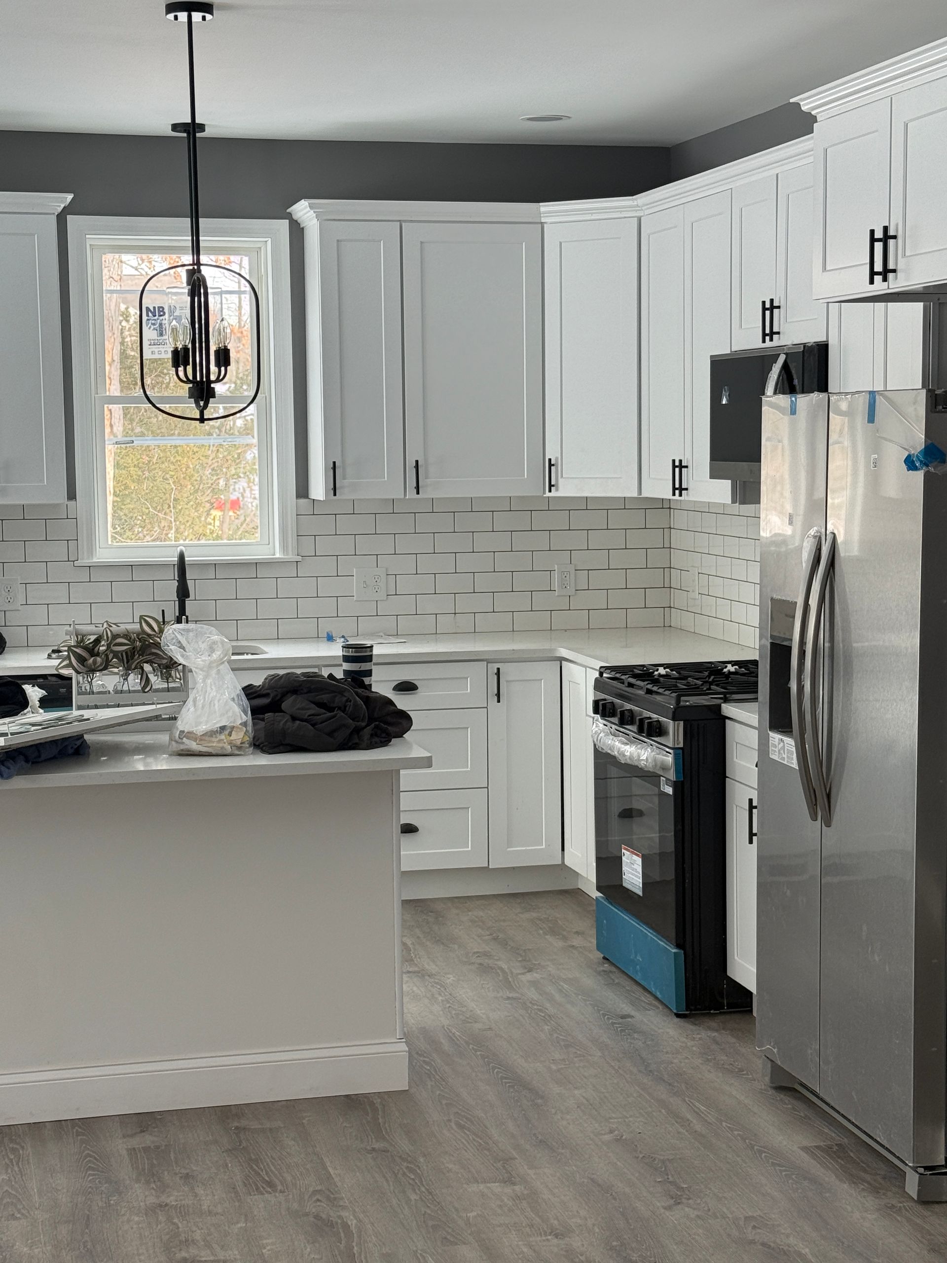 Bright white kitchen with stainless appliances, island, pendant light, and gray backsplash