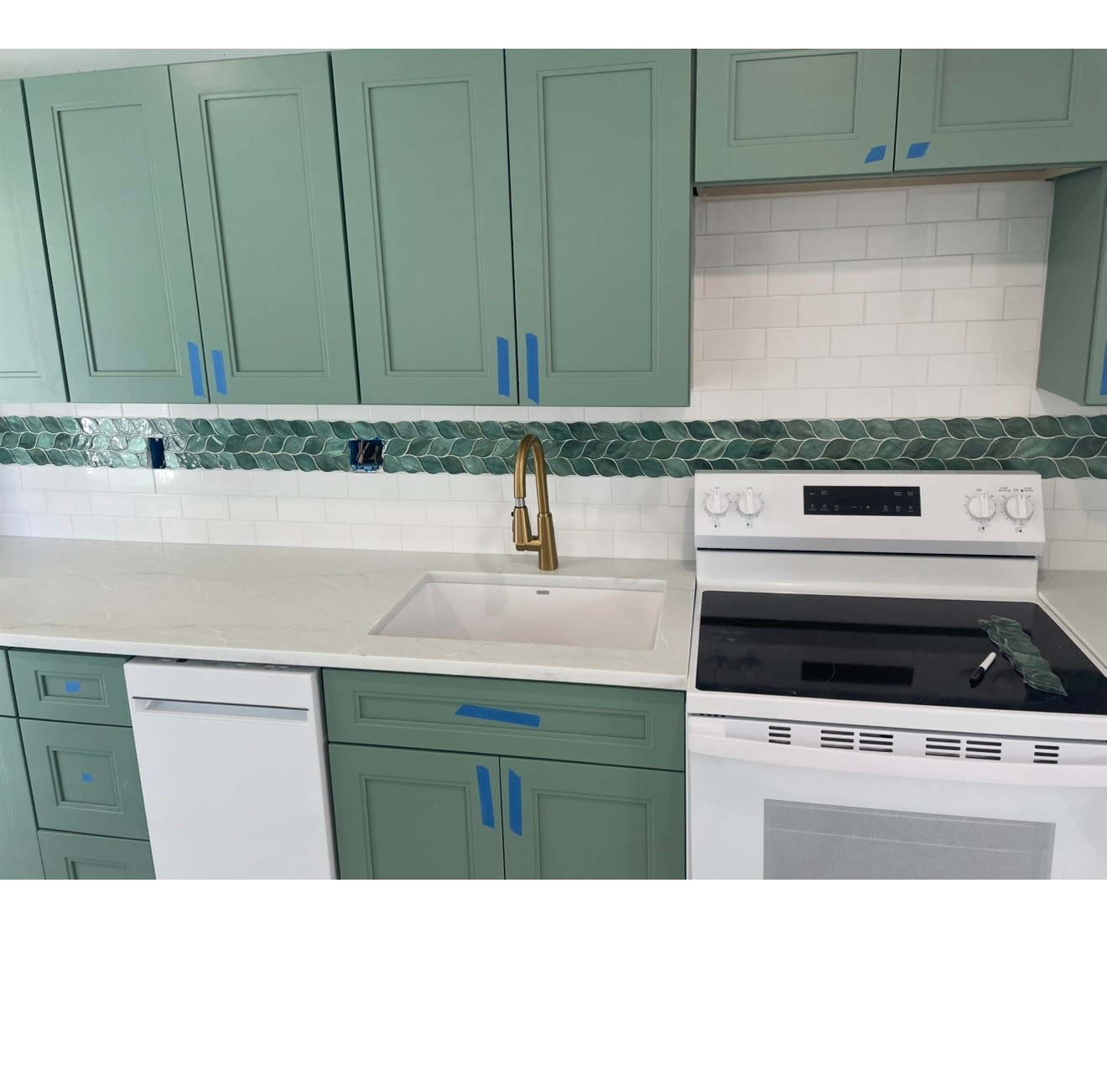 Mint-green kitchen with white countertops, brass faucet, and white stove and dishwasher