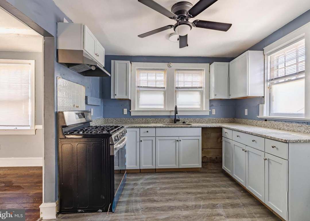 Bright kitchen with white cabinets, granite countertops, blue walls, and a ceiling fan by a window above the sink