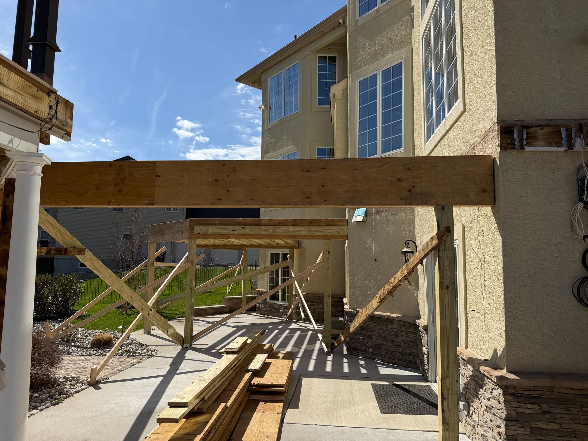 Wood-framed walkway under construction beside a stucco house with stacked lumber and diagonal bracing.