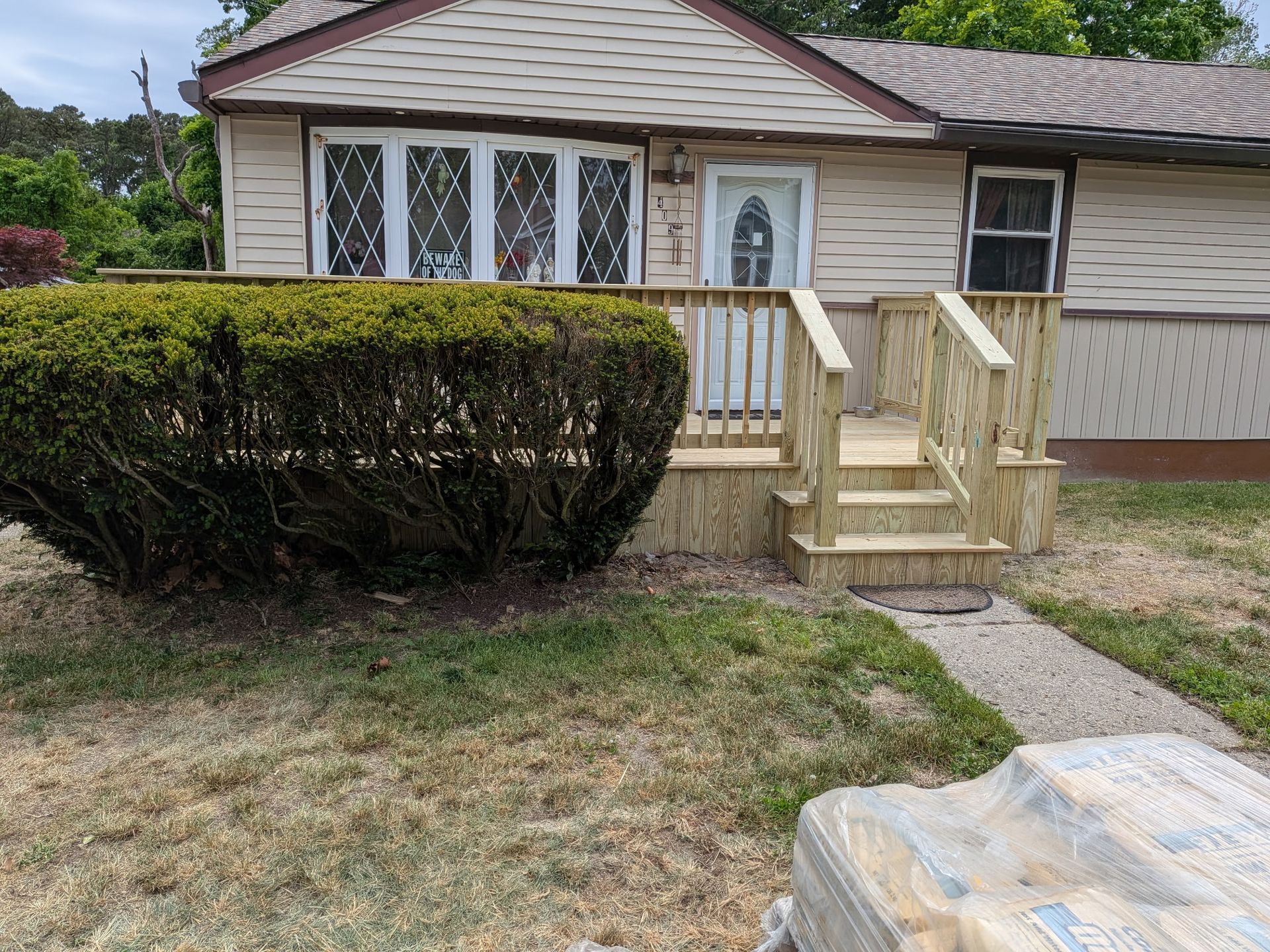 Single-story house with a small wooden porch ramp, trimmed hedge, and patchy front lawn