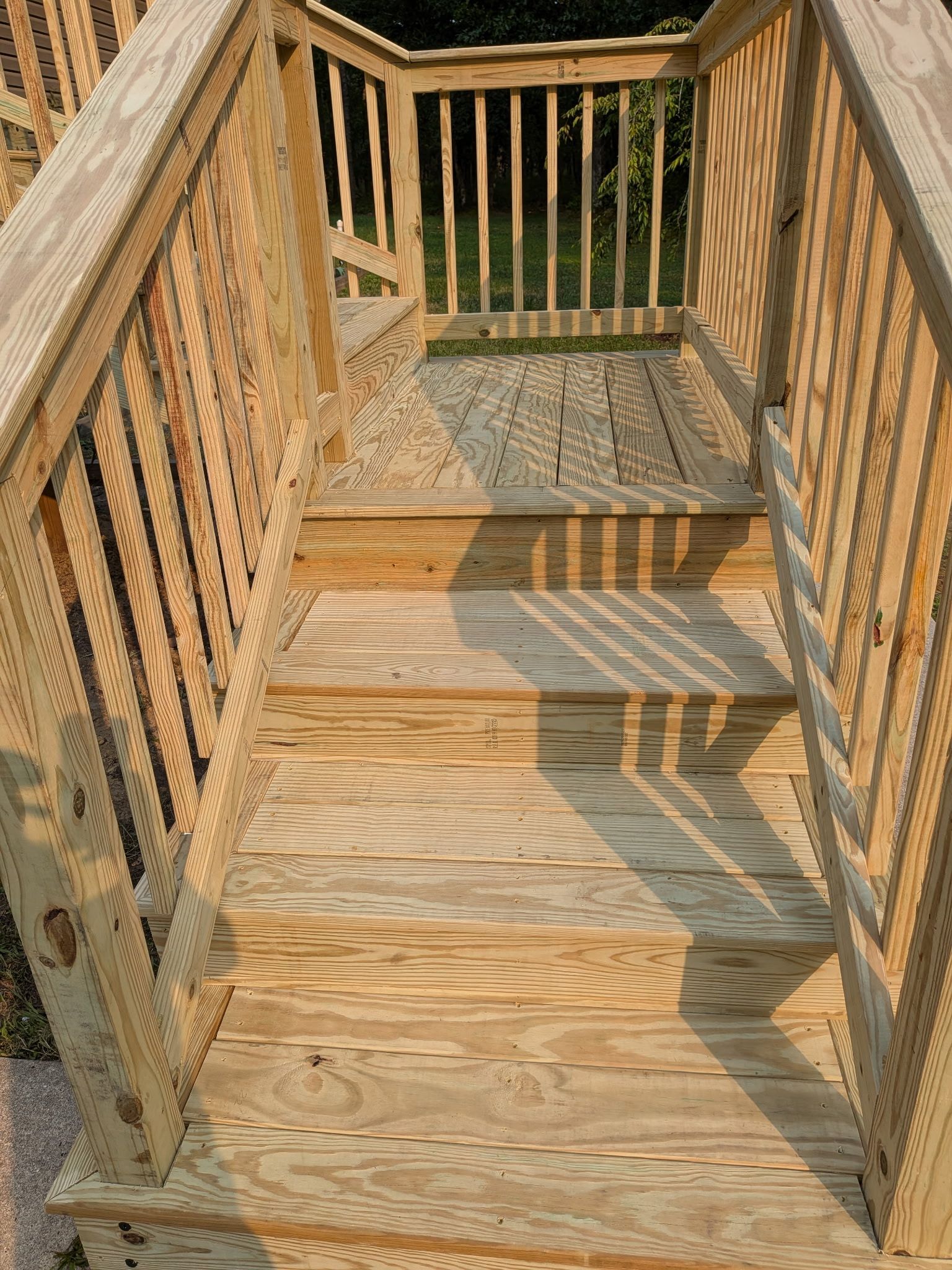 Wooden deck walkway with railings and stairs, lit by sunlight and shadows.