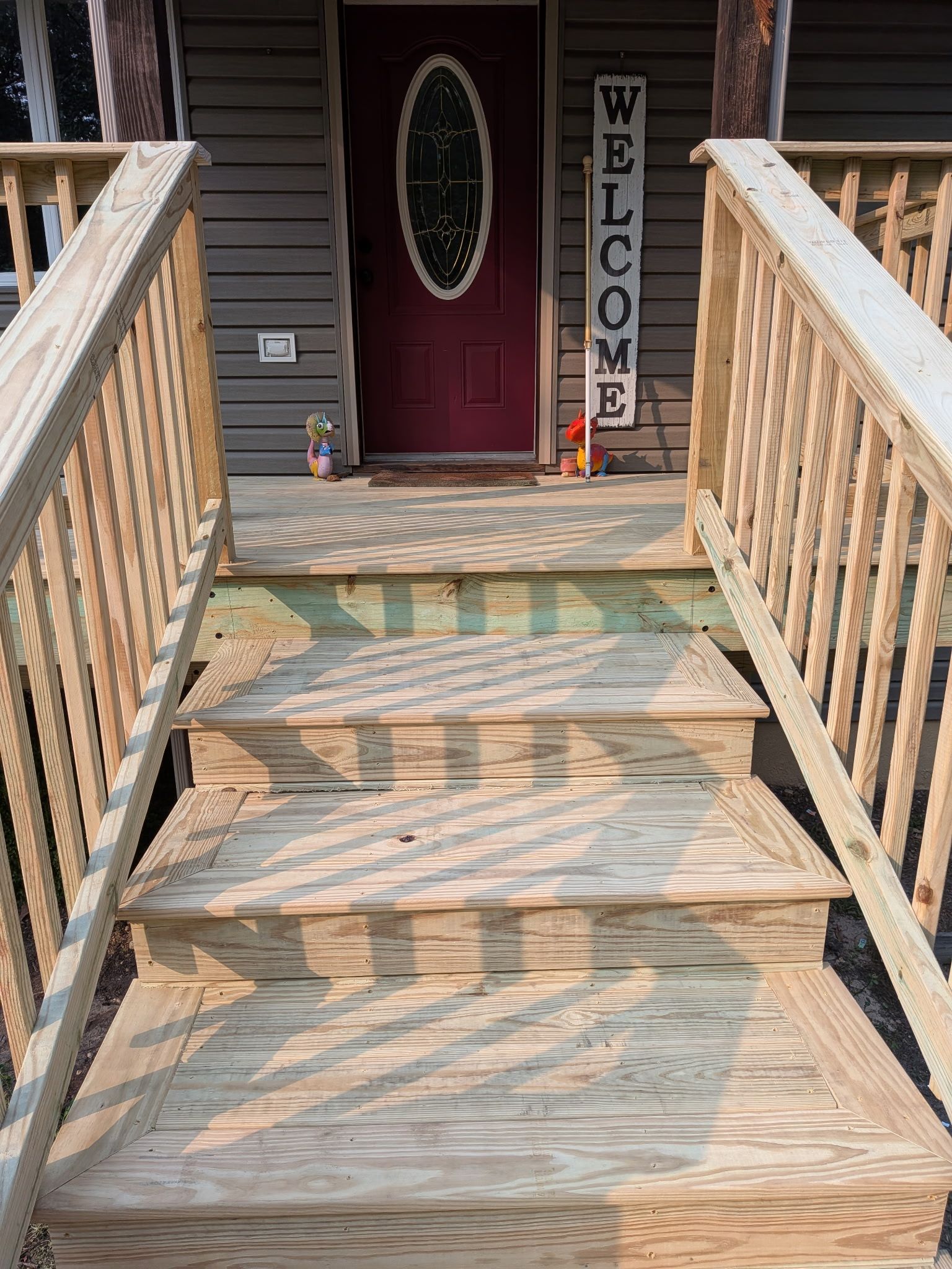 Wooden front steps leading to a porch with a red door and a vertical “WELCOME” sign