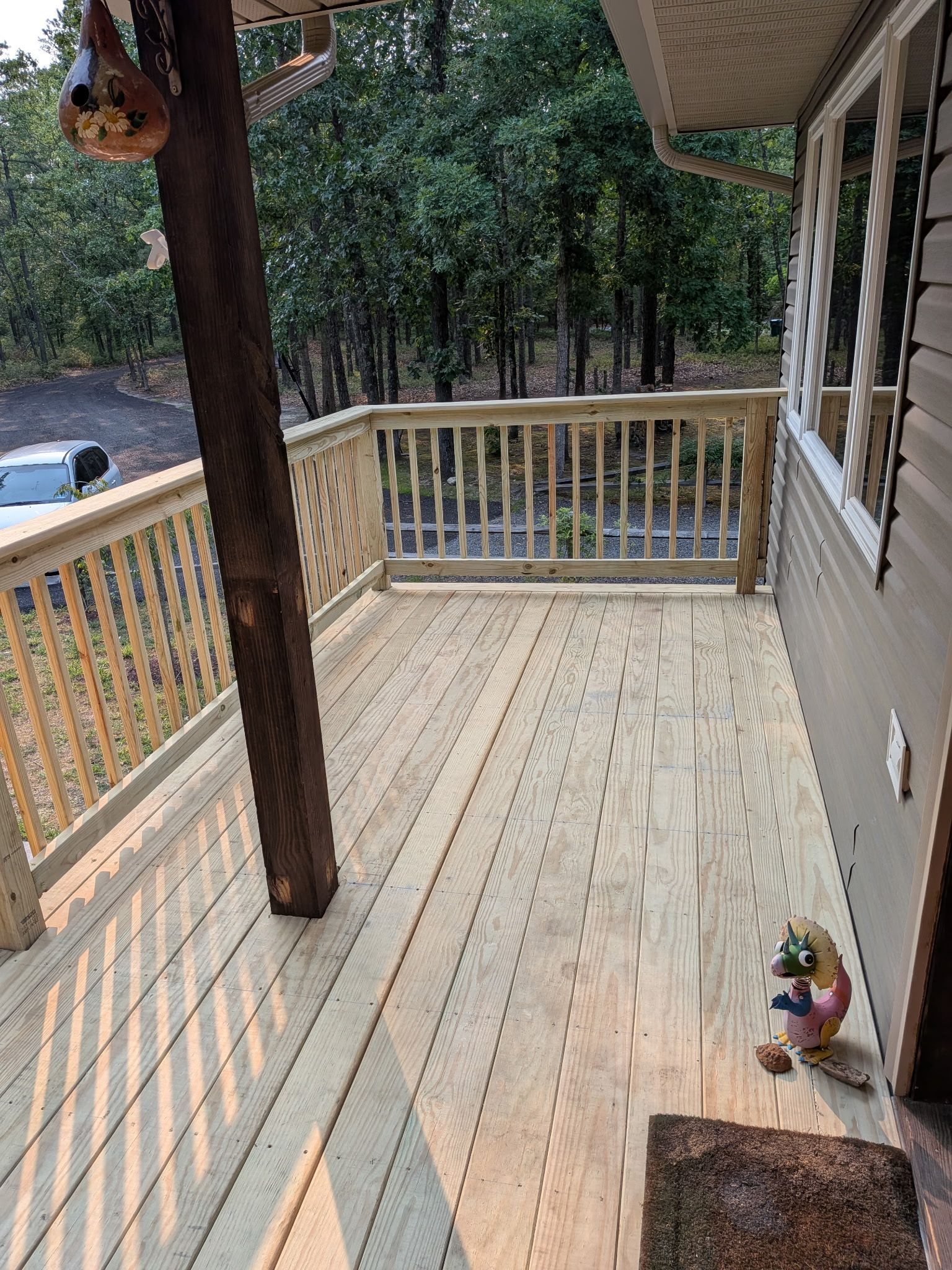 Wooden front porch with railing, trees beyond, and a small garden gnome by the wall.