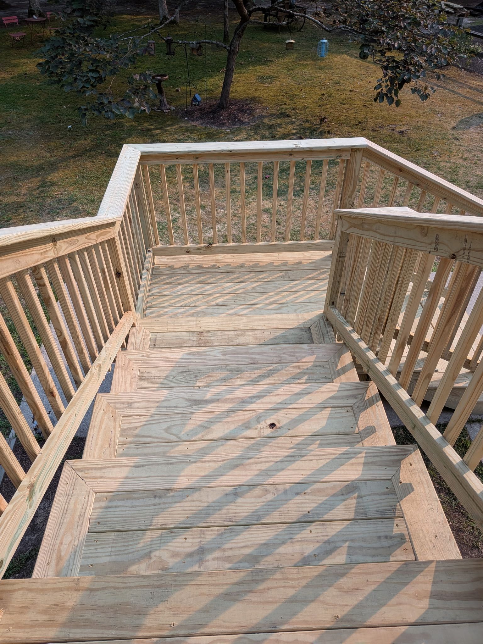 Wooden deck stairs descending into a grassy yard, with railings casting long shadows.