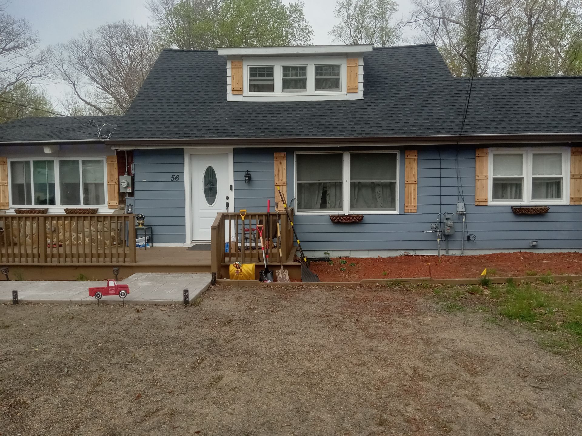 Blue house with white-trimmed windows, front porch, and a large bare yard under an overcast sky
