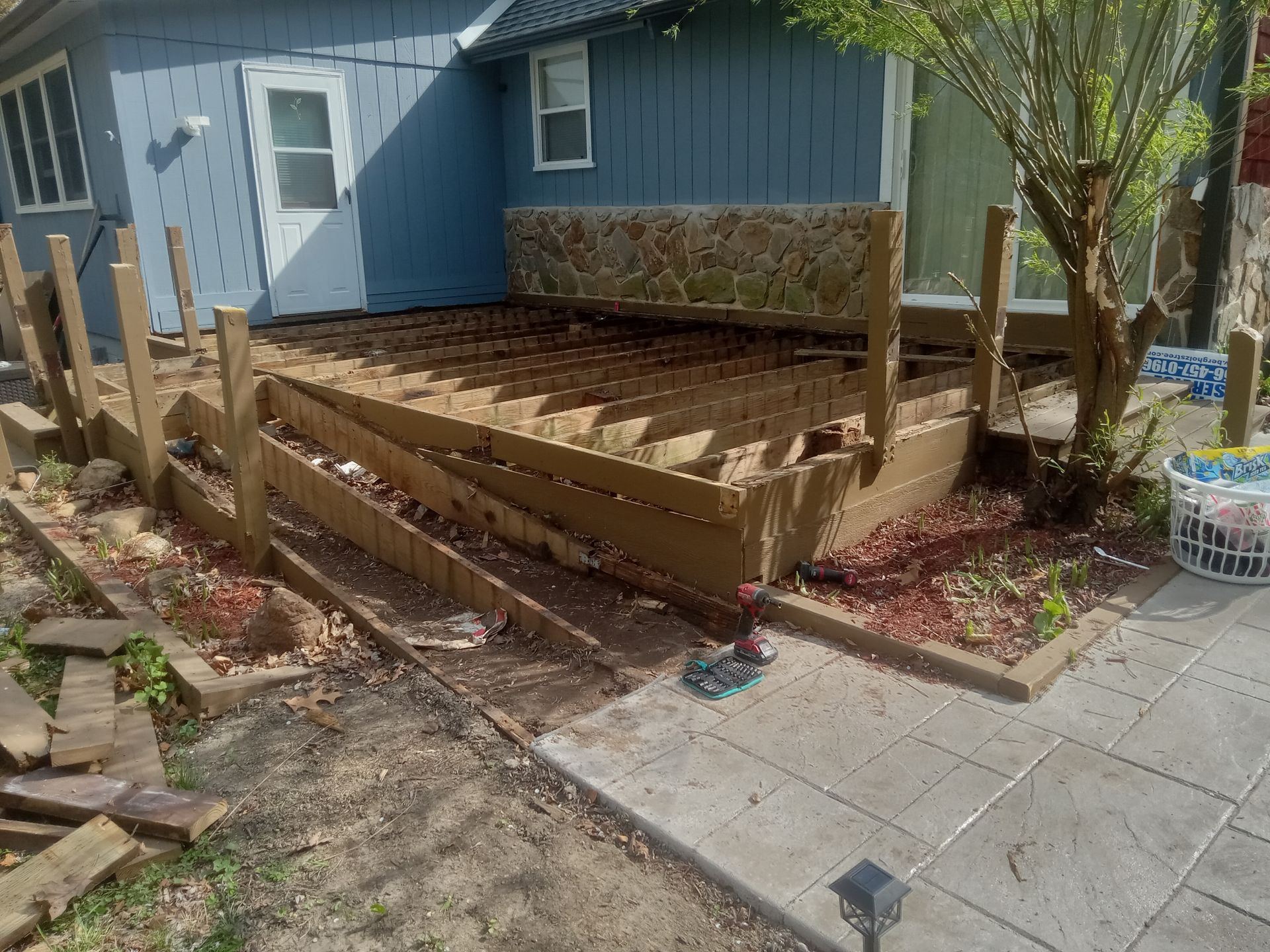 Wooden deck under construction beside a blue house, with steps and posts in a landscaped yard.
