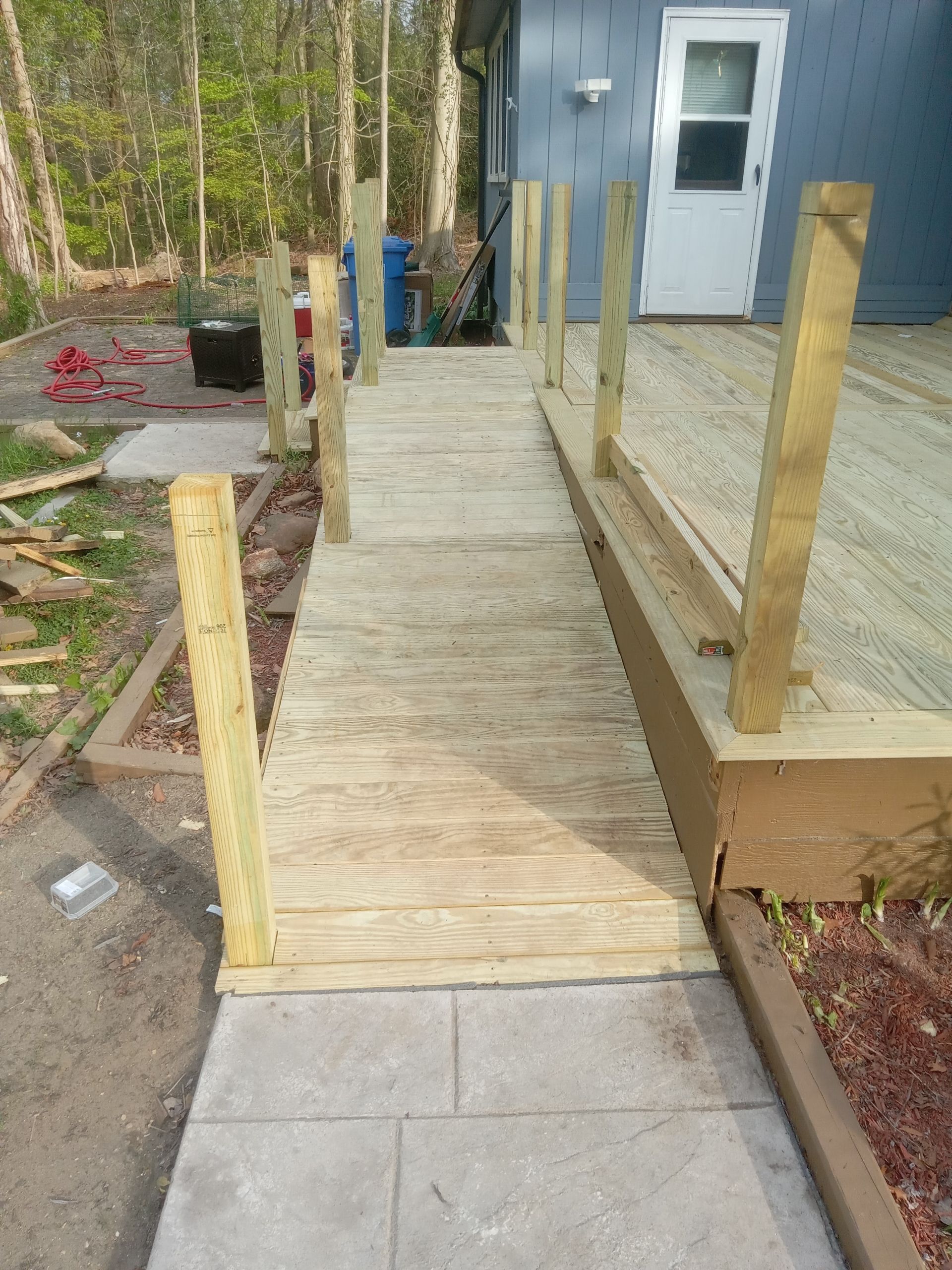 Wooden wheelchair ramp leading to a white house door, with unfinished posts and concrete walkway￼