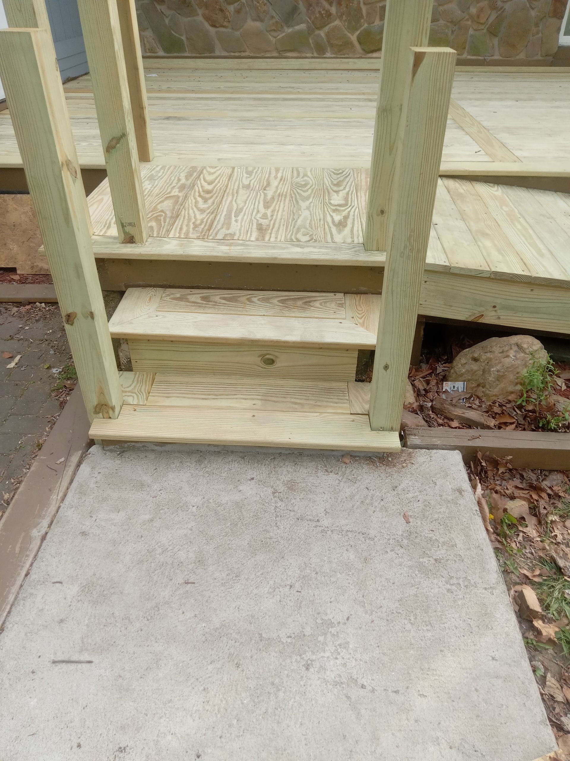 Small wooden porch steps with a short railing leading to a concrete walkway and yard.