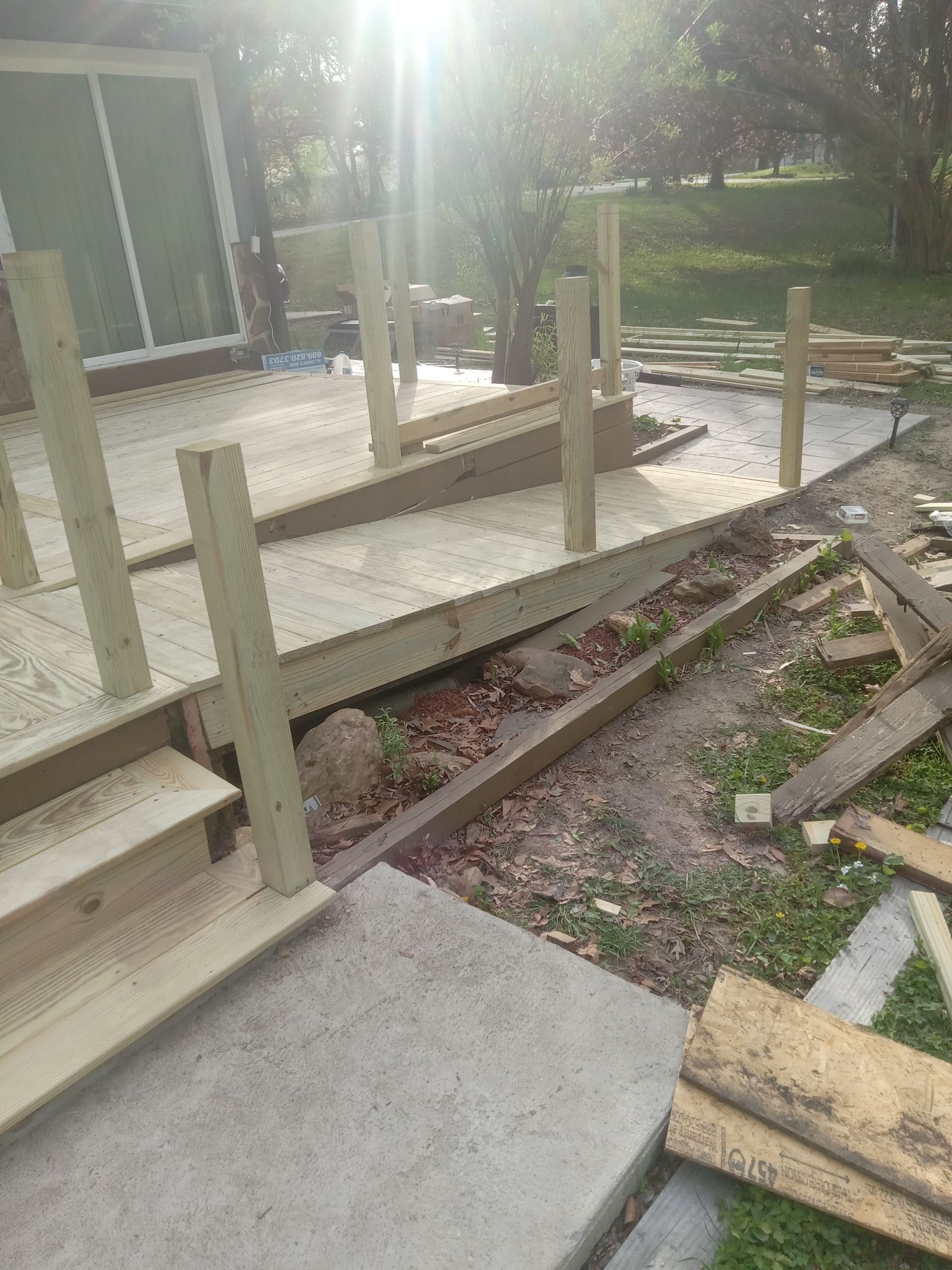 Outdoor walkway under construction with concrete ramps, wooden posts, and scattered materials beside a building
