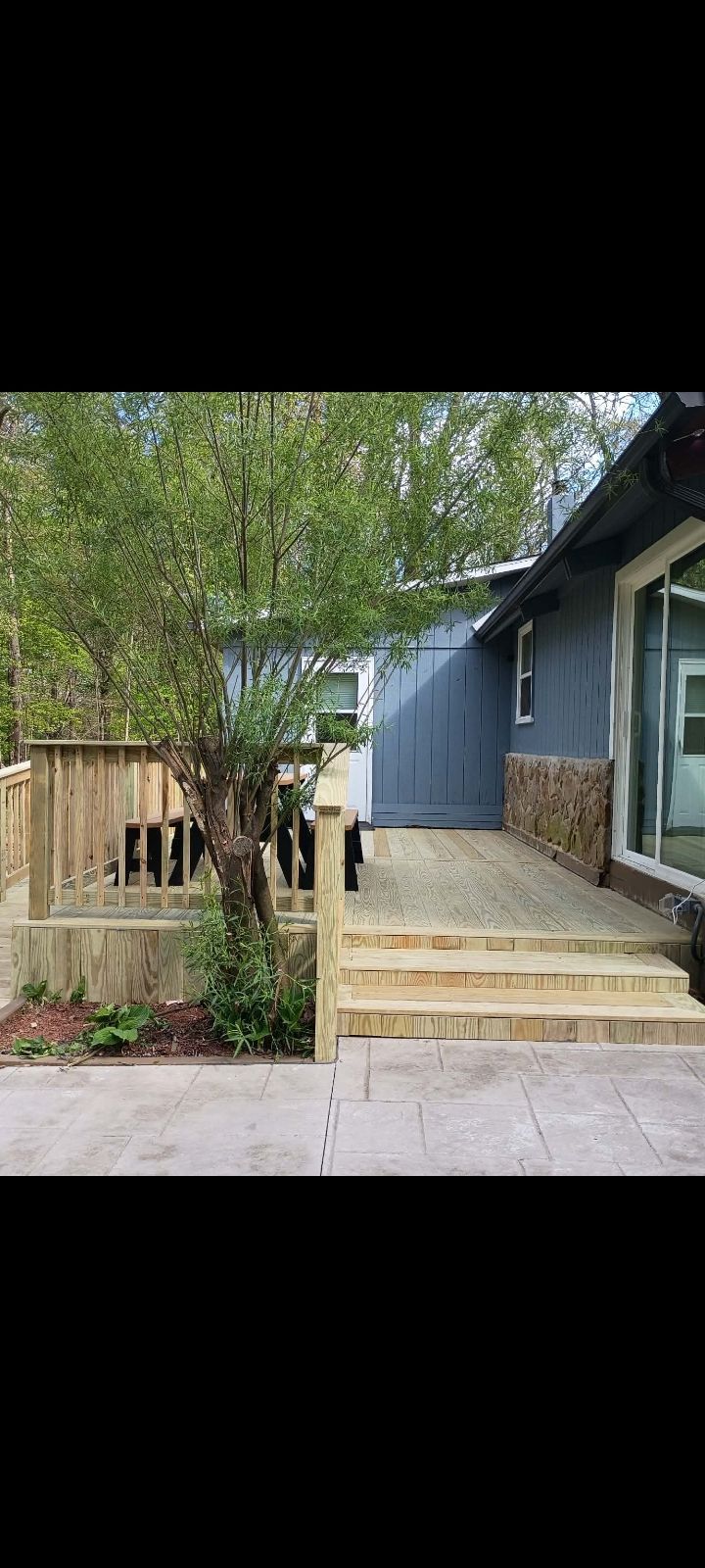 Front porch steps beside a blue house, with a tree and small garden in a fenced yard.